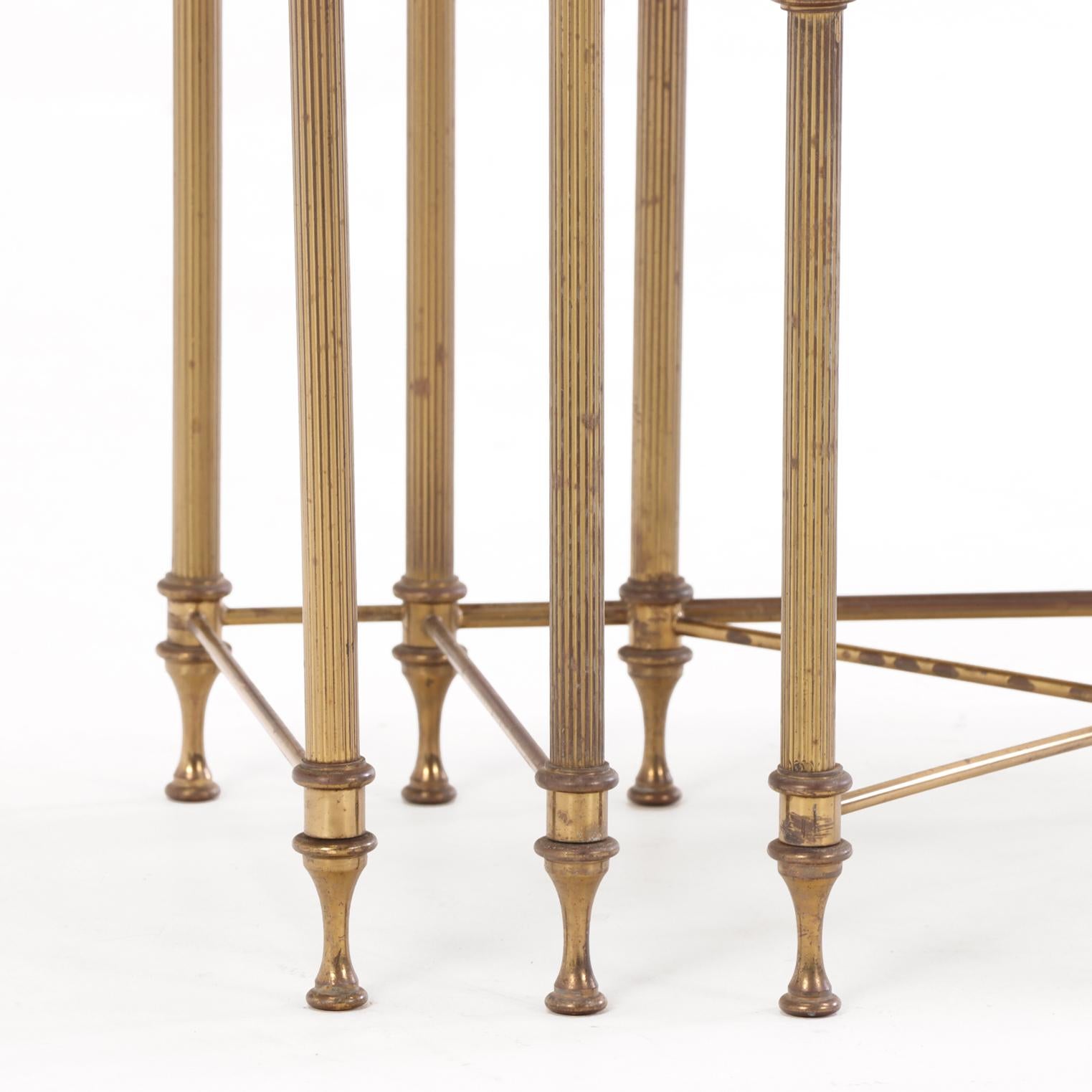 Each table features a rectangular marble top inset within a brass surround, raised on four slender supports joined at the base by stretchers.

Designed for both practicality and elegance, the tables may be stacked as a compact group or used
