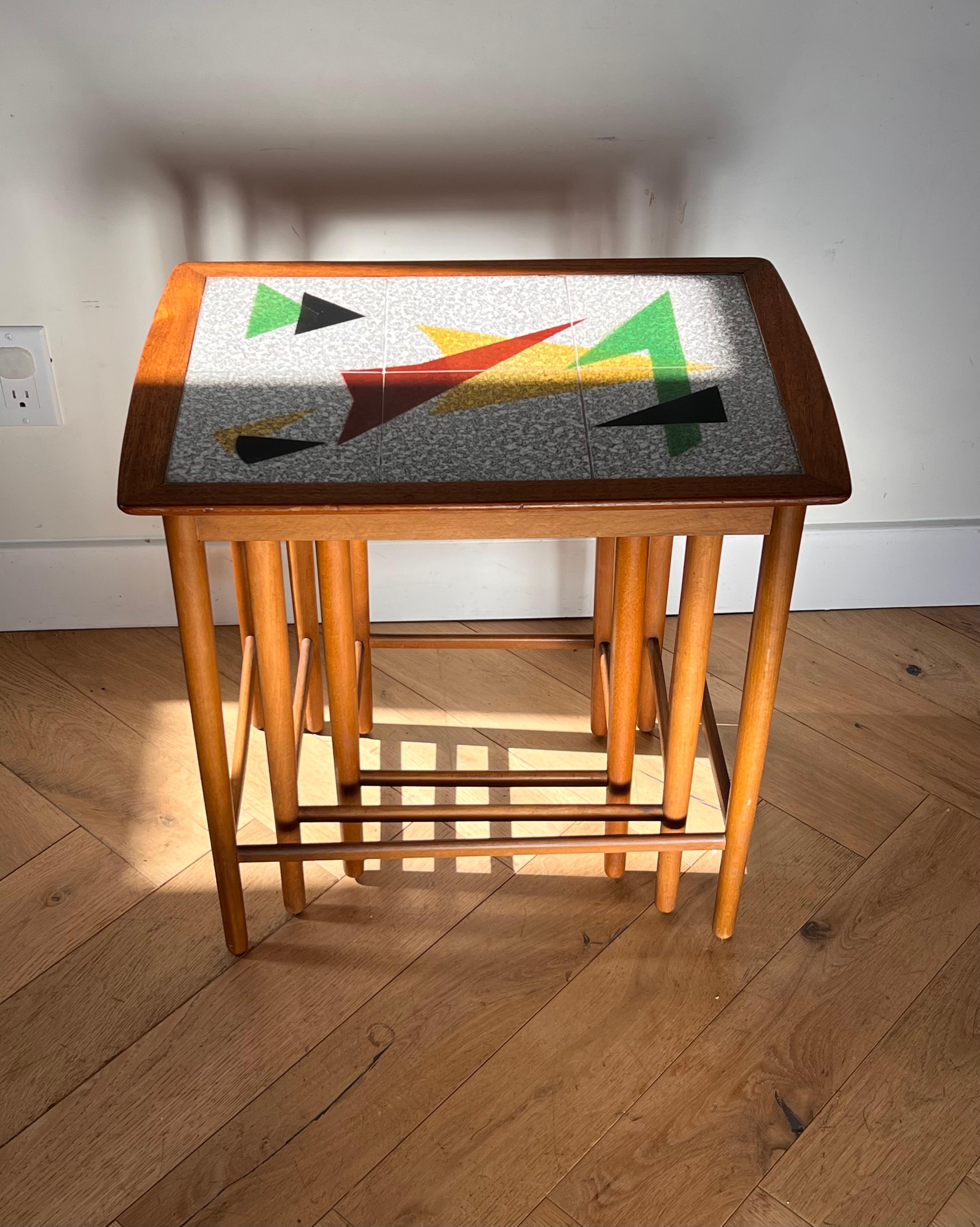 A set of three Mid century modern Danish nesting tables with ceramic tile-inlay, circa early 1960s. The richness of the teak wood contrasts beautifully with the modernist ceramic tiles which boast hues of oxblood, jet, marigold, grass green, and