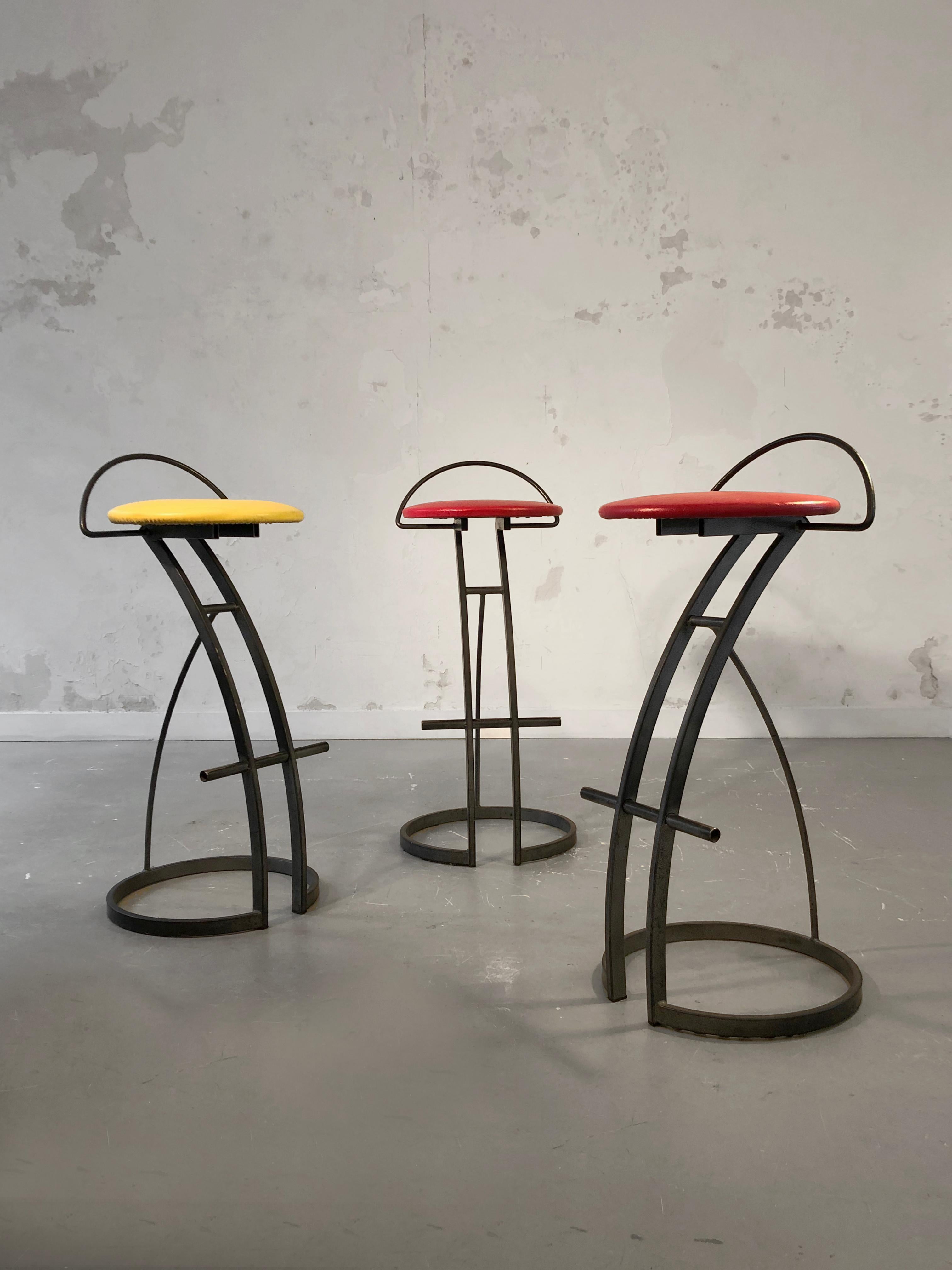 A set of 3 high bar stools, Post-Modernist, Memphis, Eighties, circular and angular structures in anthracite lacquered square section steel, footrests and low backrests, red and yellow imitation leather seats, to be attributed, France