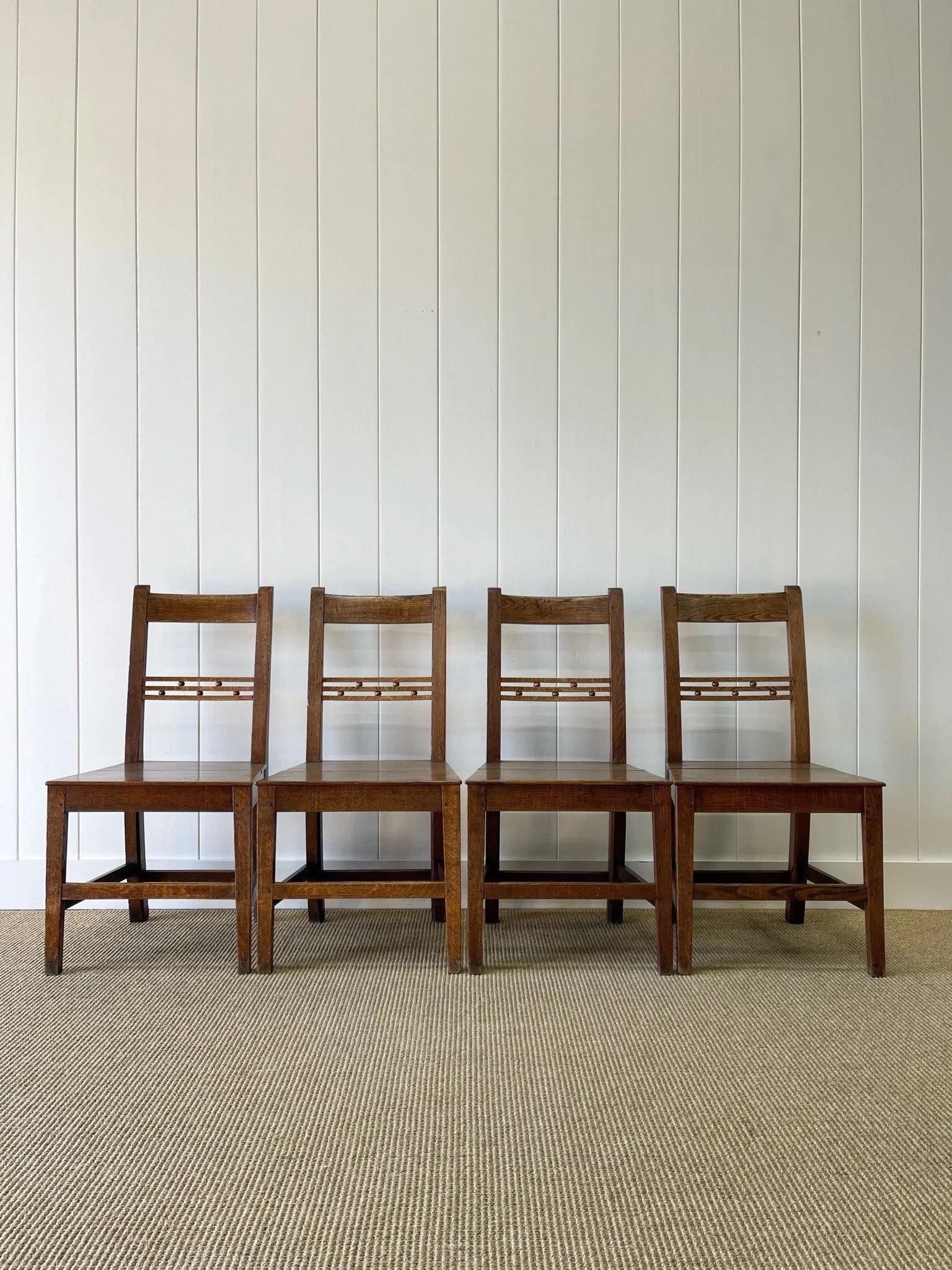 A delightful set of 4 English oak side chairs with solid seats. Lovely dark finish with good grain. Made of oak and elm. Stretchers add support. Playful orbs decorate the back splat. These are solid chairs, but should not be 