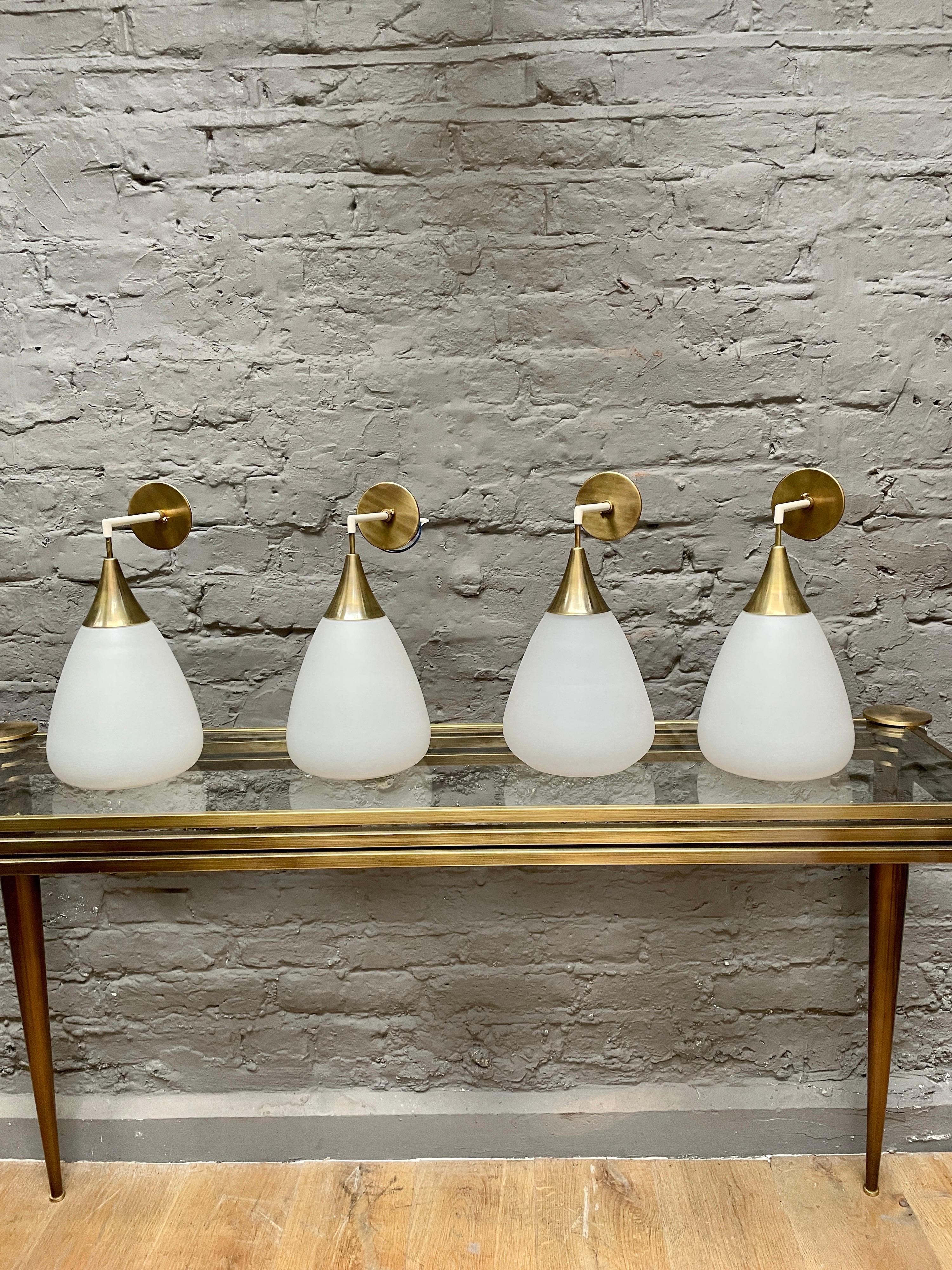 A set of four or 2 pairs of Italian brass and opaque glass wall lights. Restored and re wired with patinated brass accents, ivory lacquered supports and tear or pear shaped shades. Mid century Italian circa 1950's.