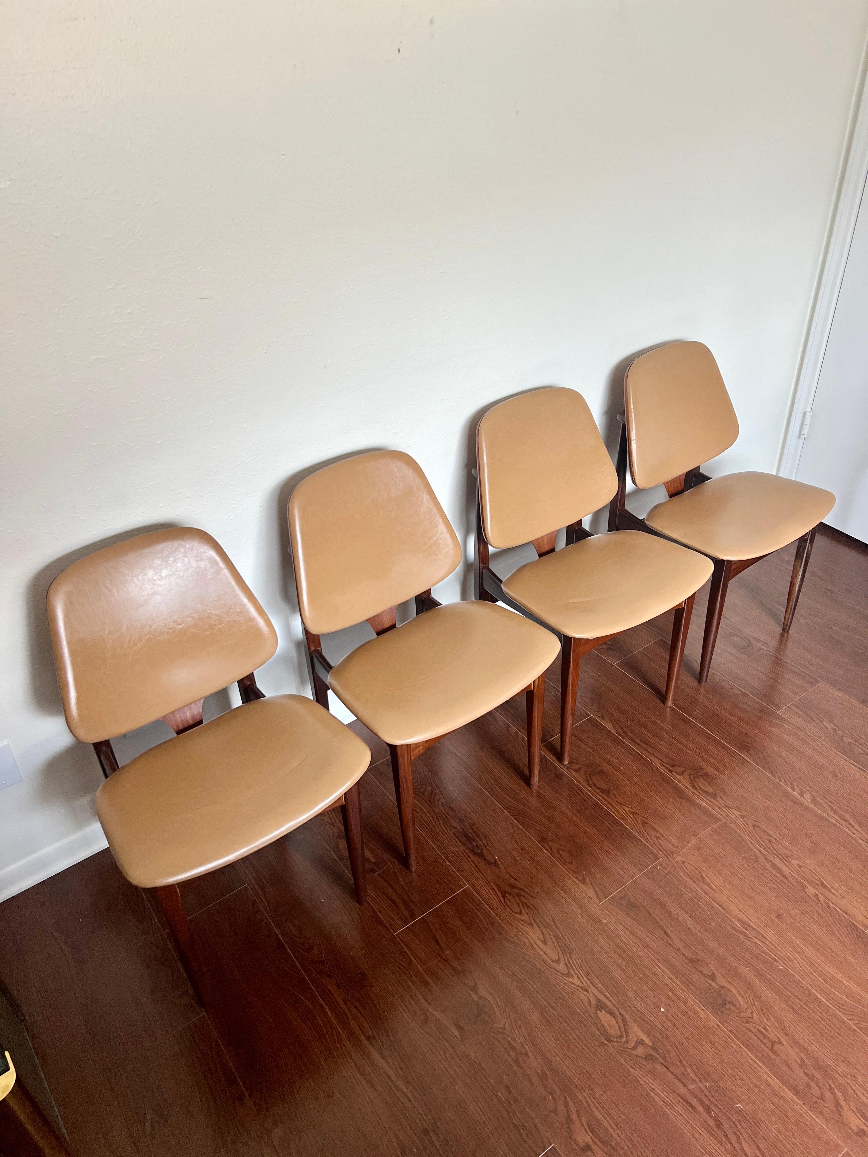 A set of 4 mid century modern dining chairs in the style of Arne Hovmand Olsen by British Maker Elliots of Newbury. These elegant teak chairs feature sculpted backs and the original vinyl seating. In very good original condition with some expected