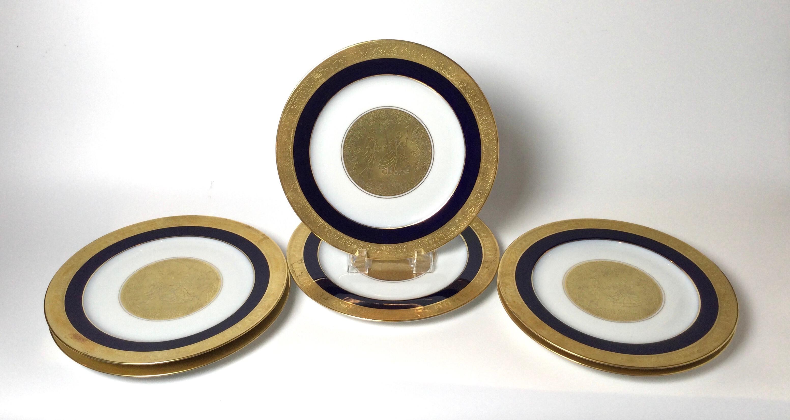 A set of 6 regal heavy gold and cobalt blue service plates. The outer broad band with cobalt band over white European porcelain with a central medallion depicting 18th century style courting couple. Measures: 10.75 inches in diameter.
