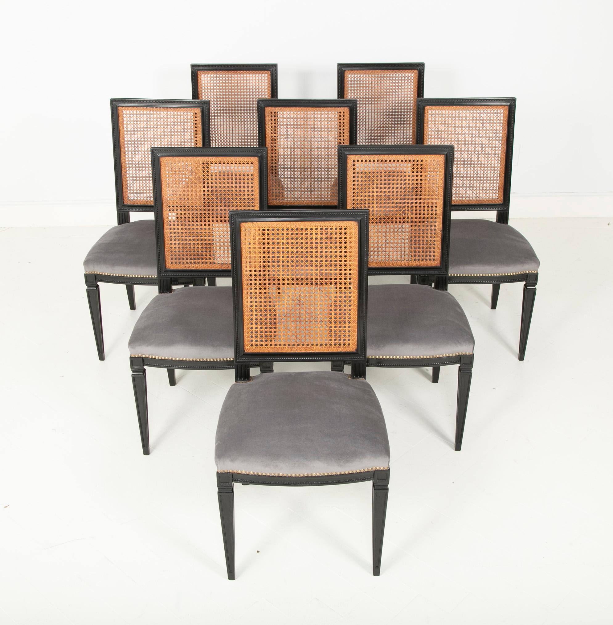 An ebonized set of 8 dining chairs with caned backs in blue/grey upholstery.