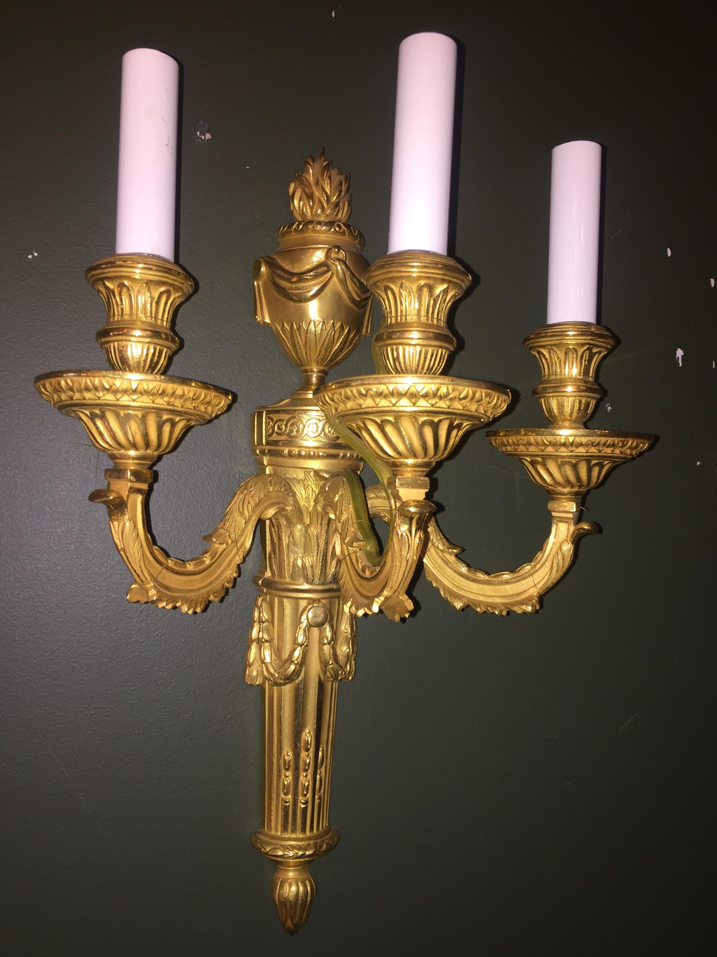 A superb set of 8  Louis XVI style gilt bronze three-arm wall light sconces of fine craftsmanship embellished with fine urns on the back adorned with flames on the top.