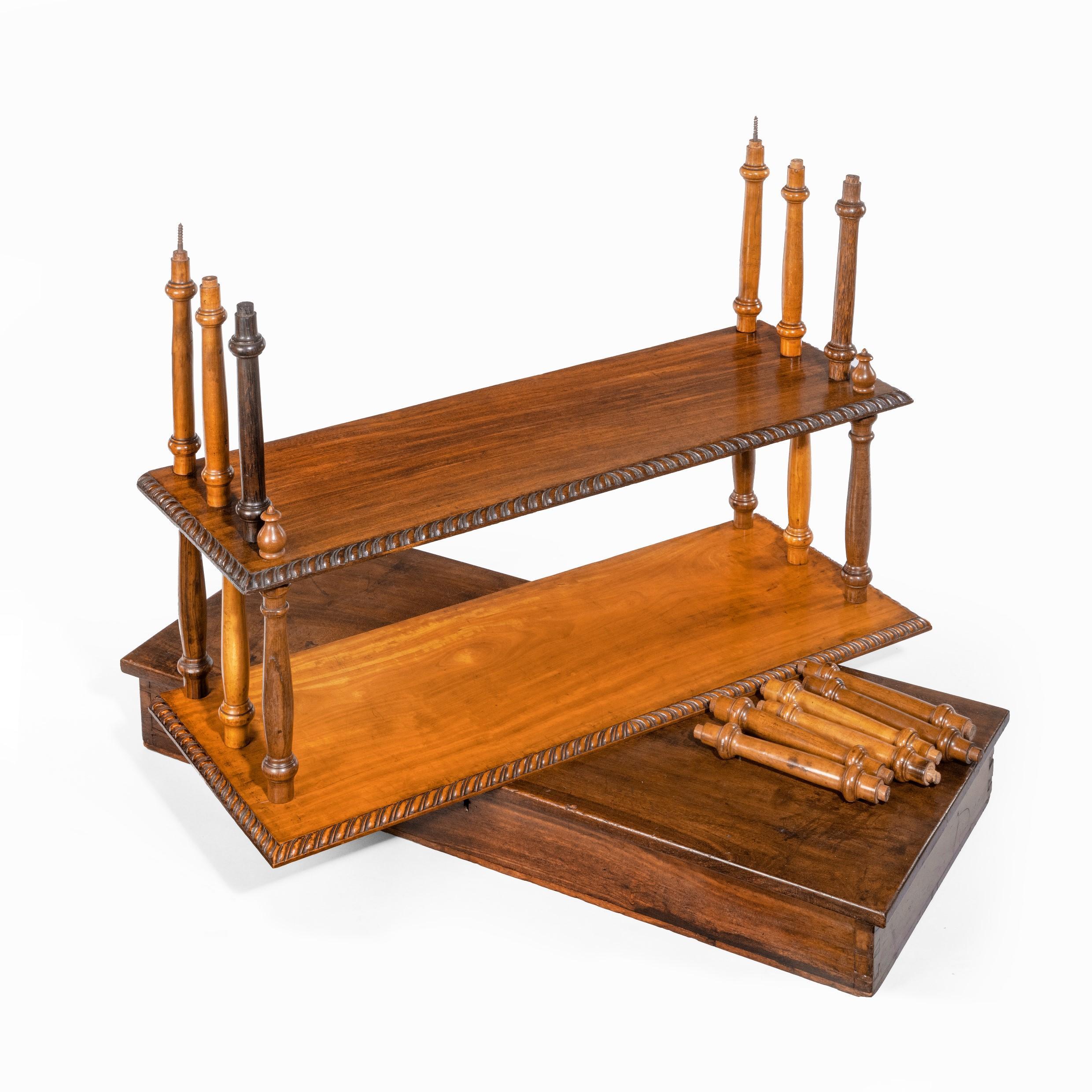 A set of Anglo-Ceylonese specimen wood Campaign wall shelves in a travelling box, of rectangular form with four graduated shelves and a carved cresting with scrolls centred on a shell, the shelves in satinwood, nedun, kadumberiya and sappoo, with