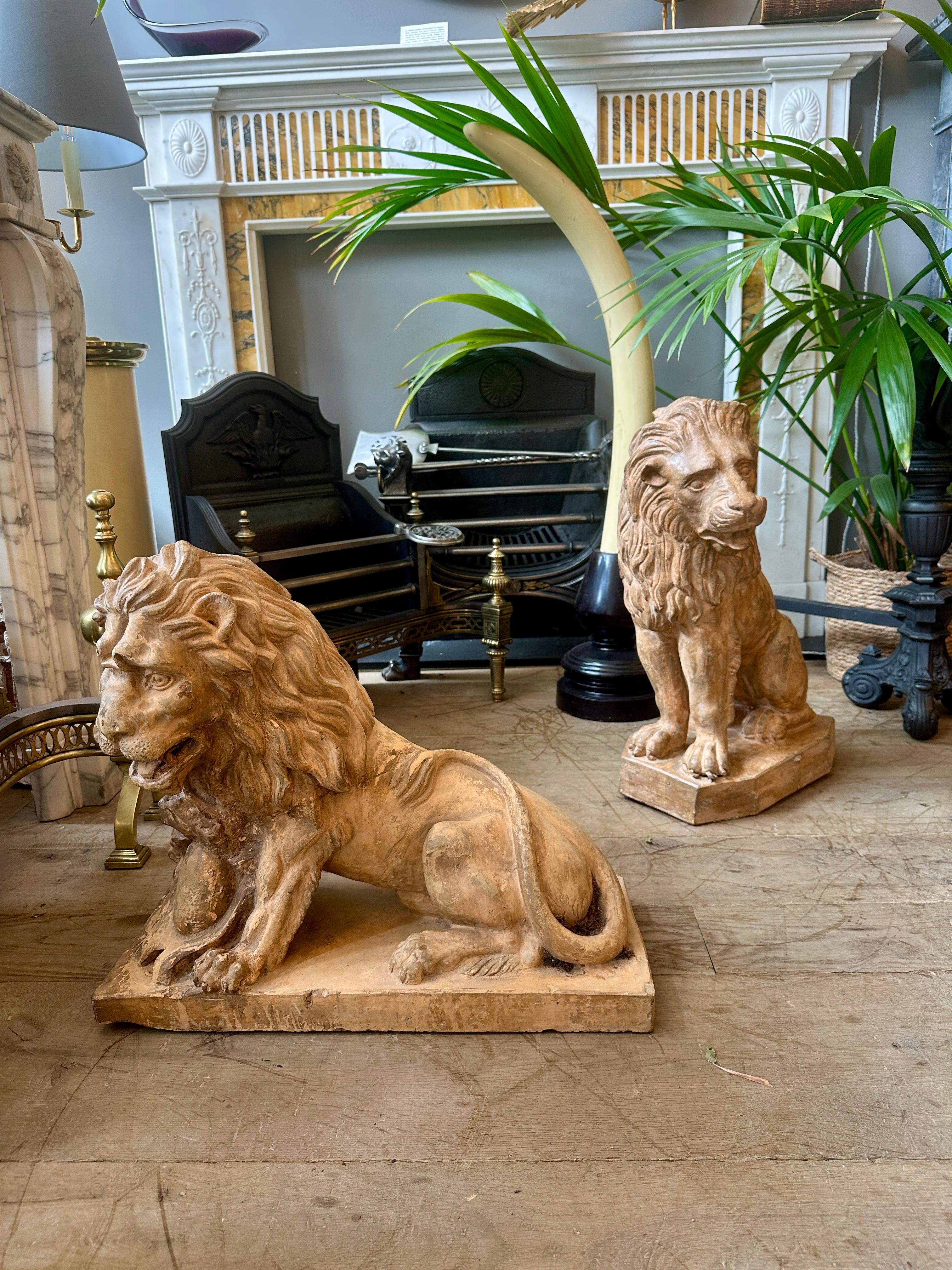 A Set of European 19th century terracotta lions. One seated stood on a shaped plinth, expressive face, detailed mane and muscular form. The other recumbent, shield bearing with detailed mane and facial expression. Both with original untouched