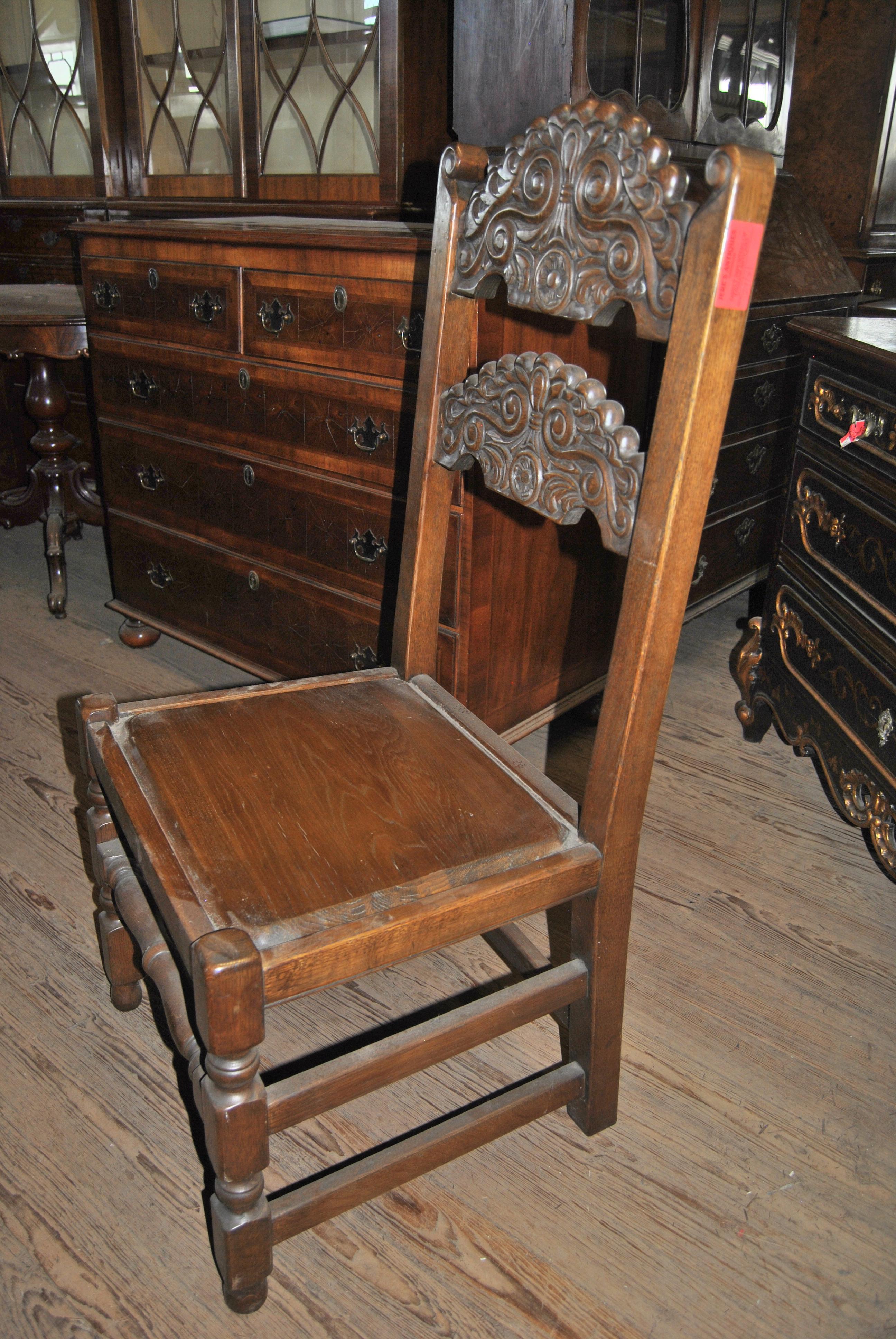 This is a matched set of 8 side chairs, in the Jacobean style, made in England, circa 1920. The chairs are made of solid oak. The back uprights curl over at the top of each chair. There are 2 heavily and finely carved splats across the back of each