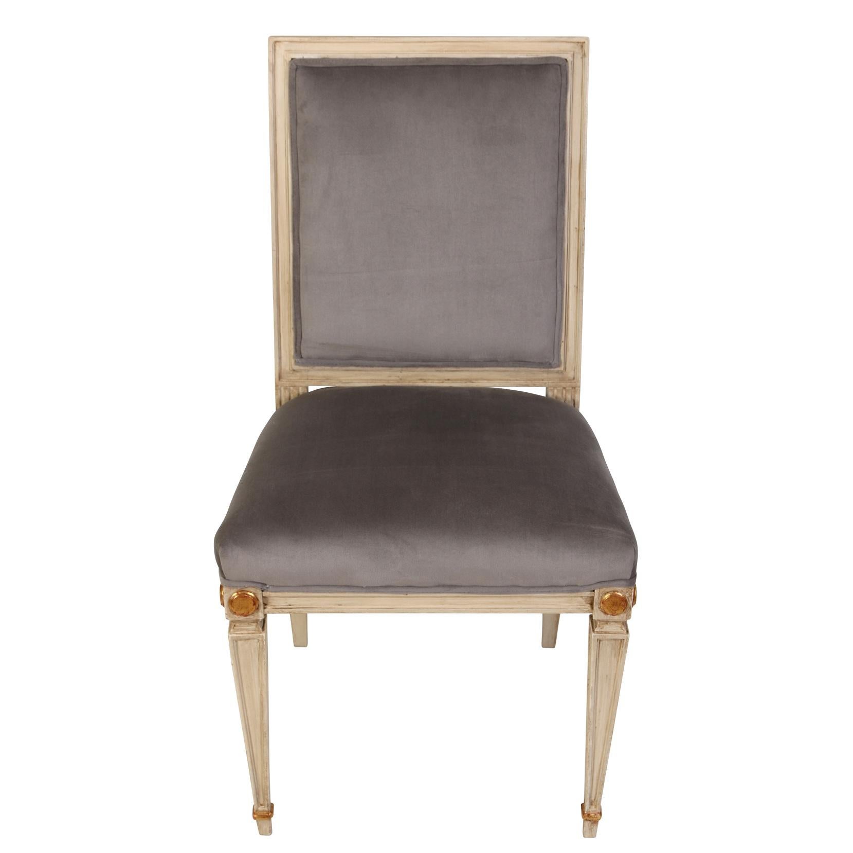 We love the understated elegance of these Louis XVI style dining chairs. Painted in a light gray finish, the chairs have a squared back and seat. The legs are squared and tapered with brass sabots and the frame features subtle gold leaf accents.