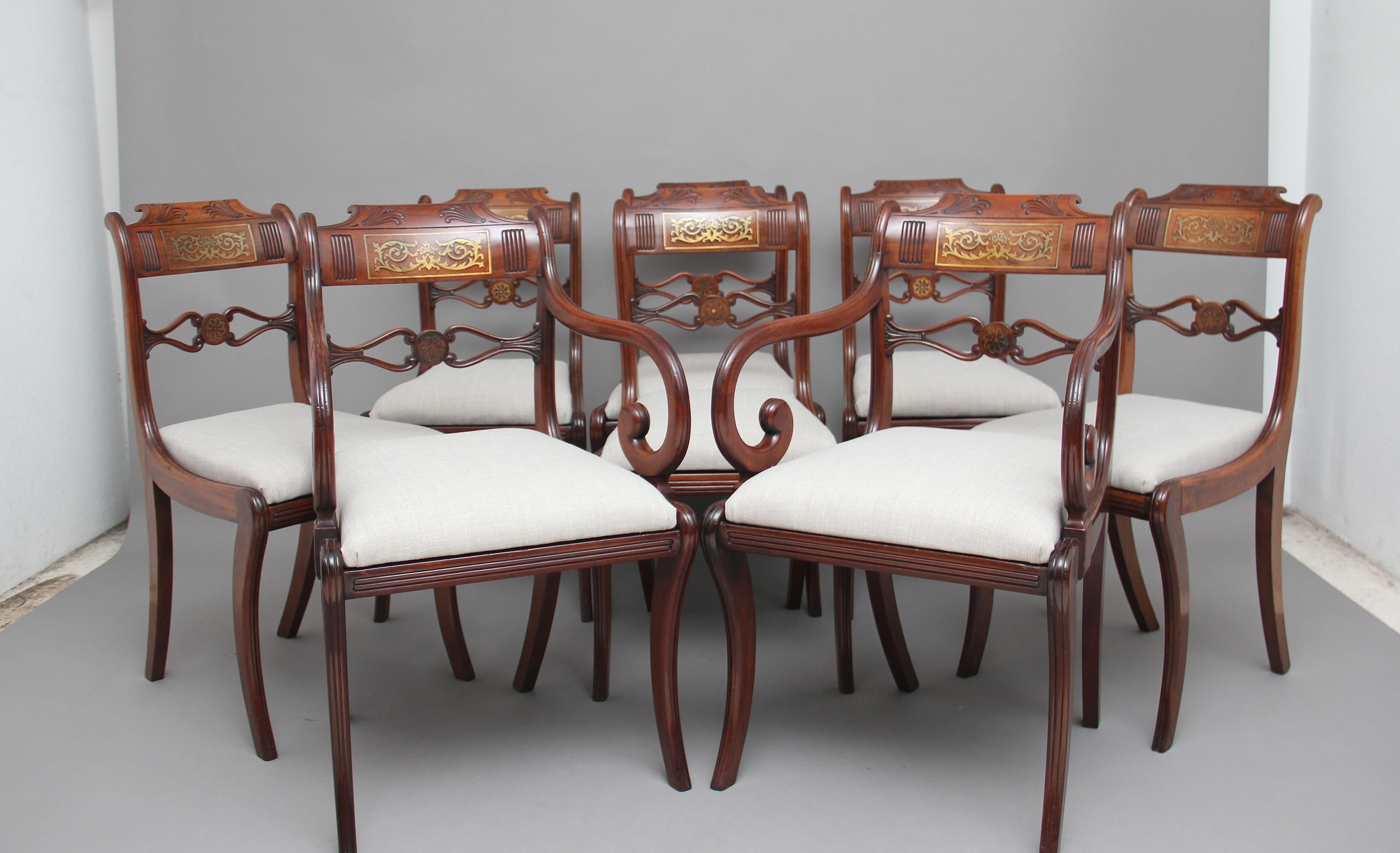 A set of eight Regency mahogany and brass inlaid sabre leg dining chairs, consisting of six side chairs and two armchairs, the shaped top rail carved and having a brass inlaid panel, wonderfully shaped and carved central rail, the armchairs having