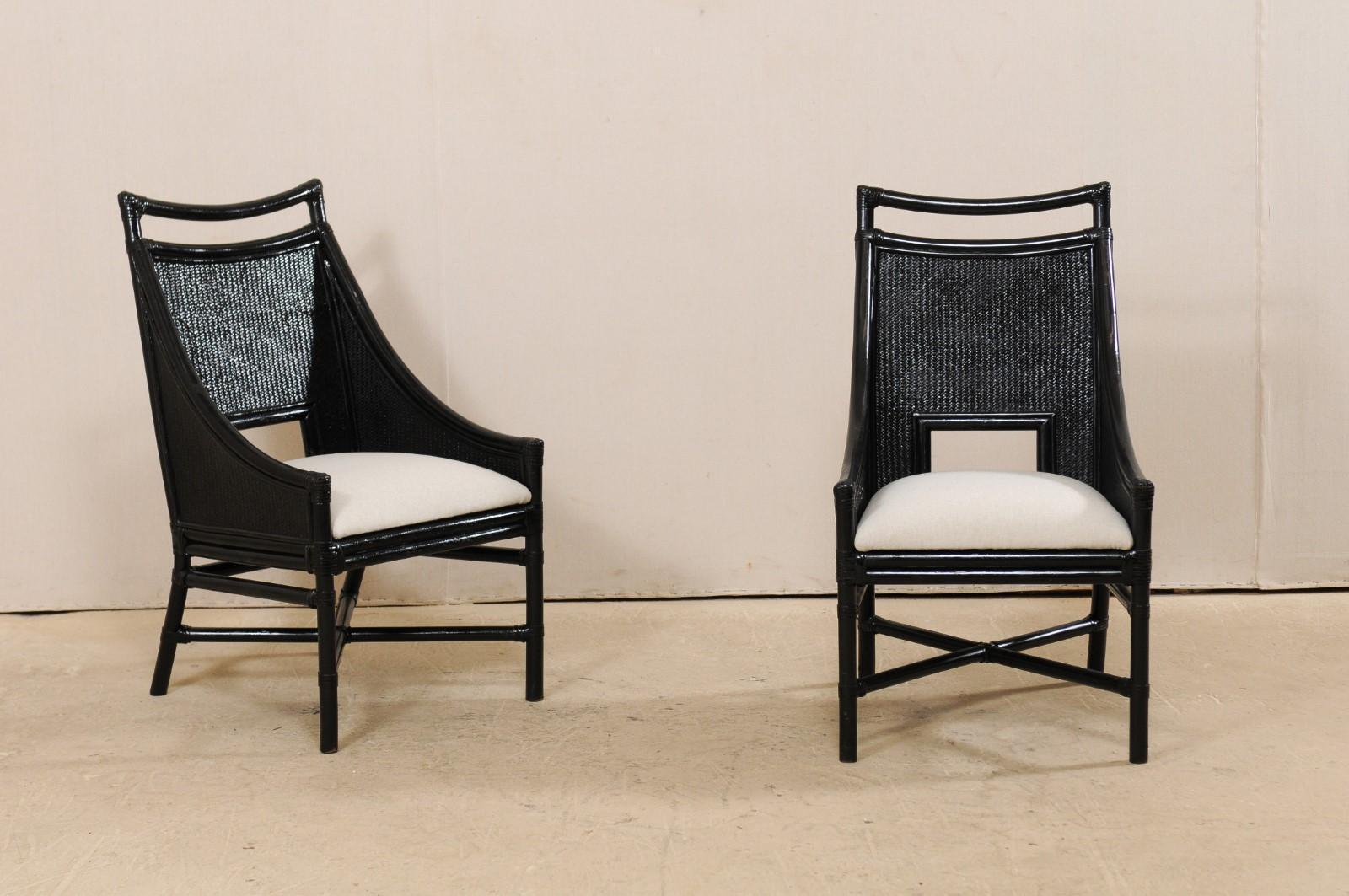 A set of 8 vintage American painted bamboo and cane chairs with upholstered seats. These vintage side chairs have a modern aesthetic to them with their sloping arms, back cut-outs, and shiny black finish. The chair backs have a swagged raised top