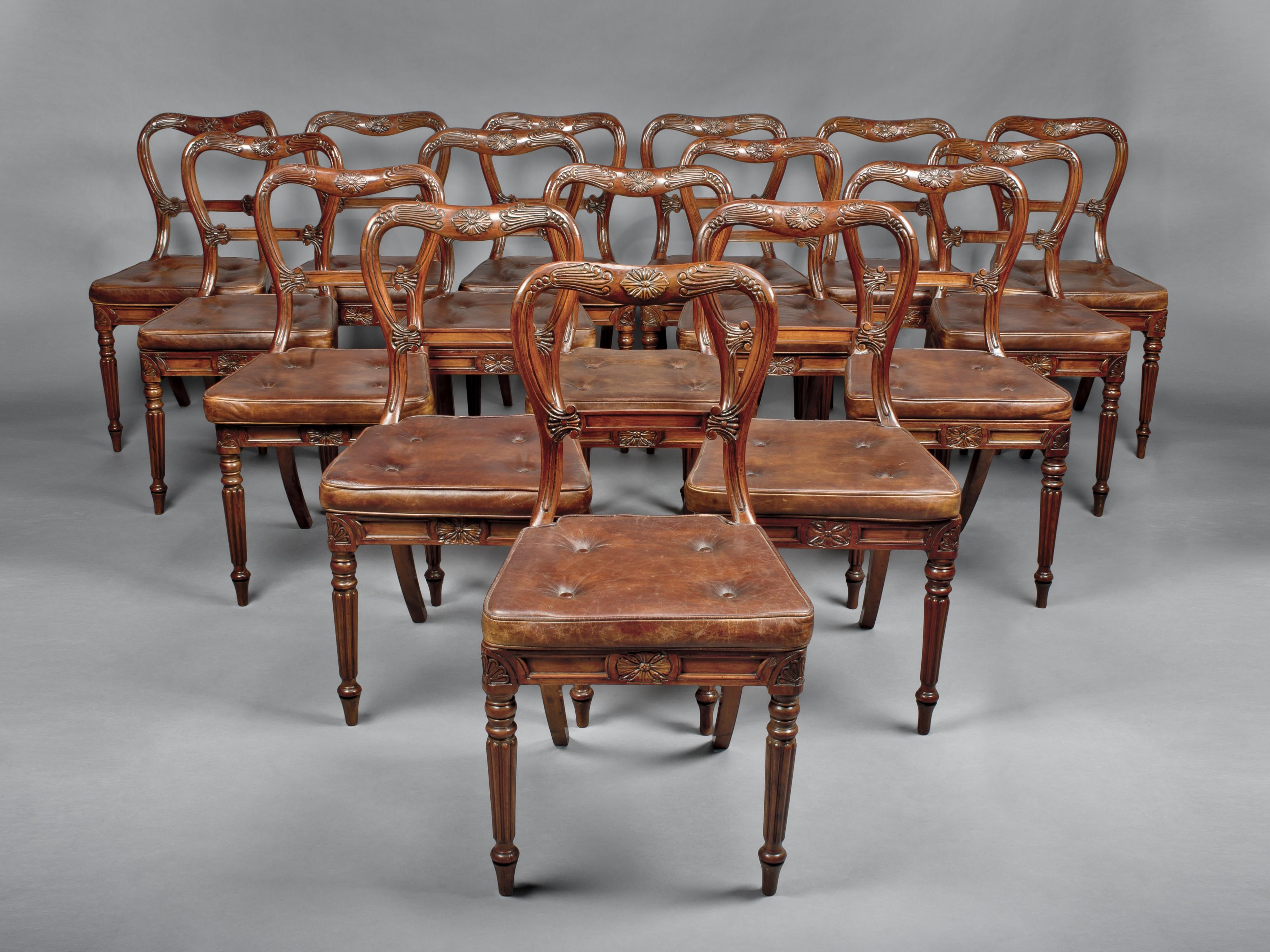A set of eighteen red walnut dining chairs attributed to Gillows. 

English, circa 1830.

Each chair has a waisted balloon back, with incised foliage and panelled horizontal splat, above a caned seat and panelled apron centred by a flowerhead,