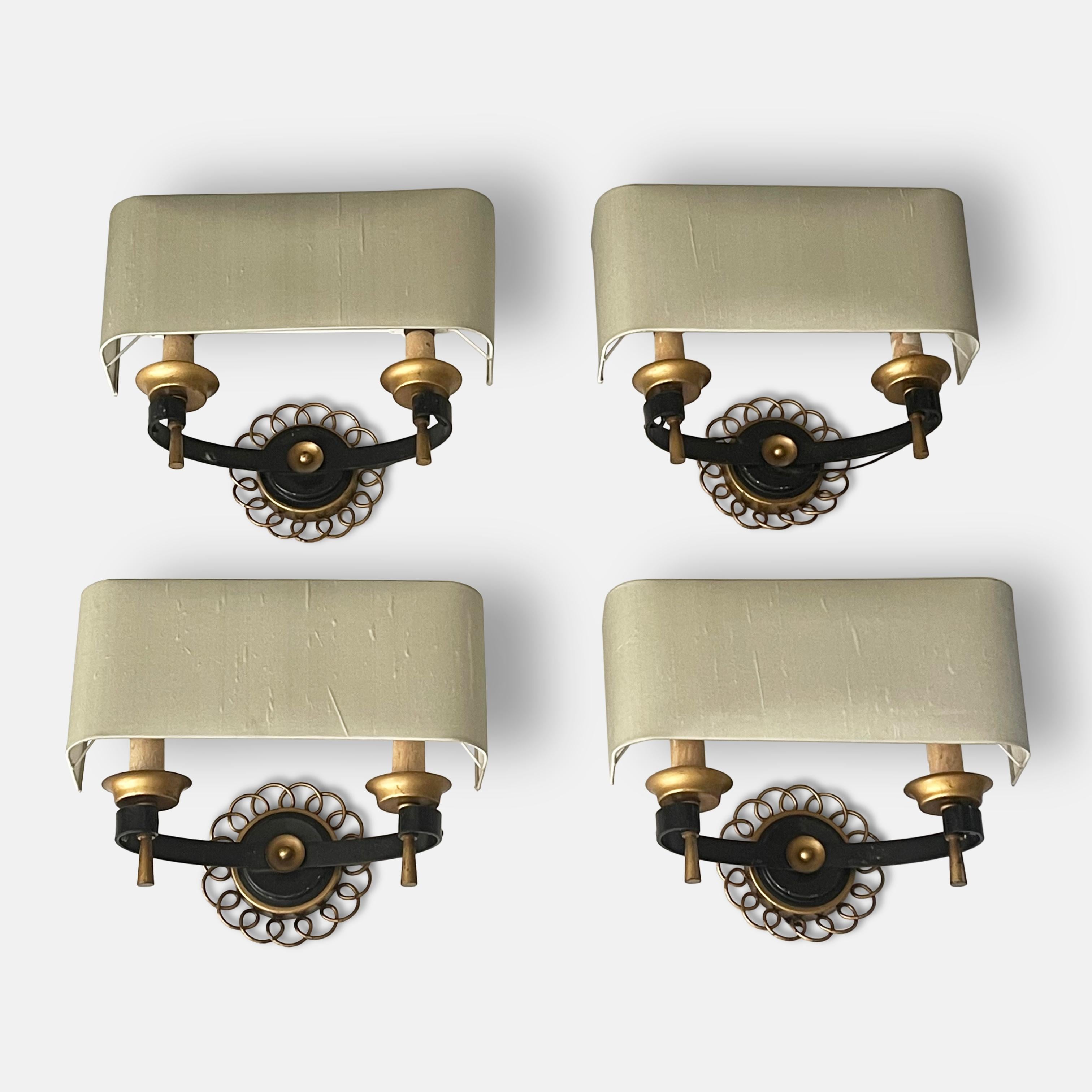 A set of four 1940s French wall lights in the style of Gilbert Poillerat.

A beautiful set of four wall lights each with a double bulb and stylish wrap around silk shades. A semi-circular arm with a scrolled end each hold a torche set off by a