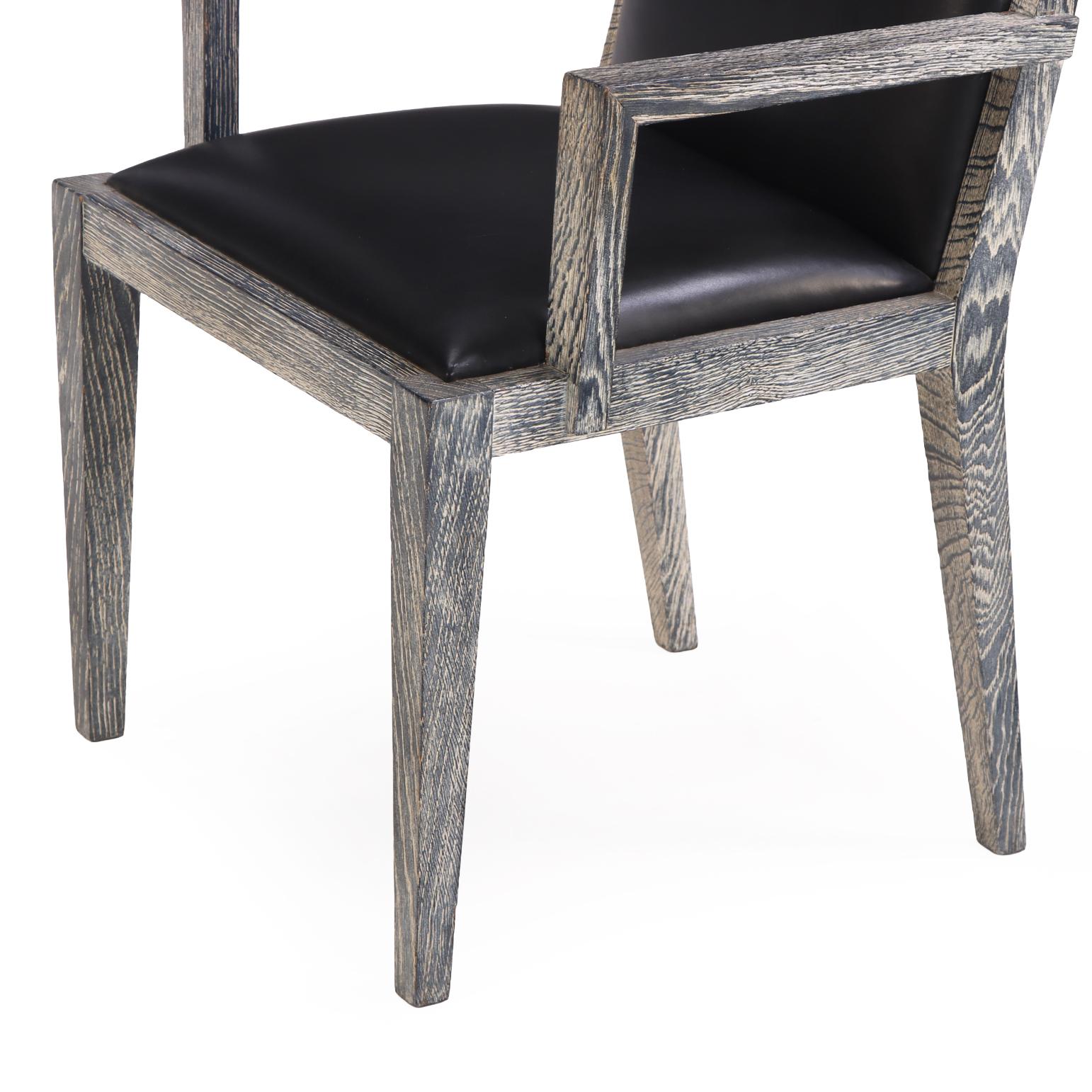 A sleek set of four French armchairs in cerused oak, the frames feature clean, angular lines that highlight the dramatic grain of the cerused finish. Each chair has a comfortably scaled seat and backrest upholstered in smooth black, creating a