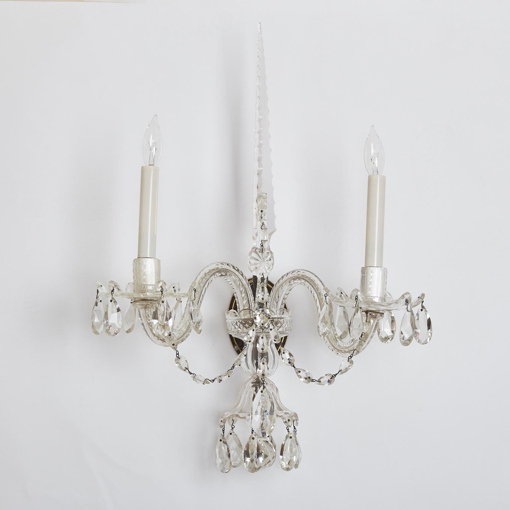 A set of four two-light George III style sconces with obelisk-shaped finials and crystal arms. Each elegant light fixture features bobeches and candle cups draped with crystal beads, circa 1890.
 