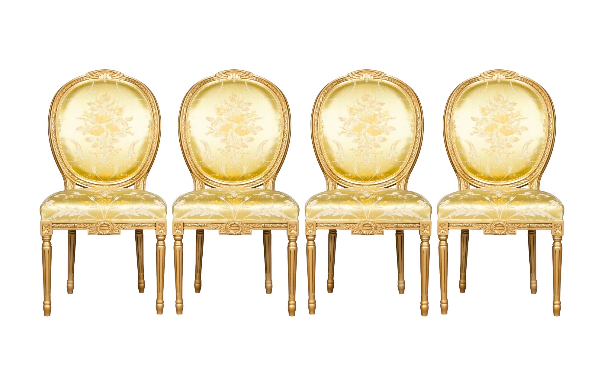 This set of four Italian Louis XVI style dining chairs exemplifies timeless elegance and craftsmanship. Each chair features a gilt wood frame with a tablet back, adorned with hand-painted floral and foliate carvings. The fluted legs are topped with