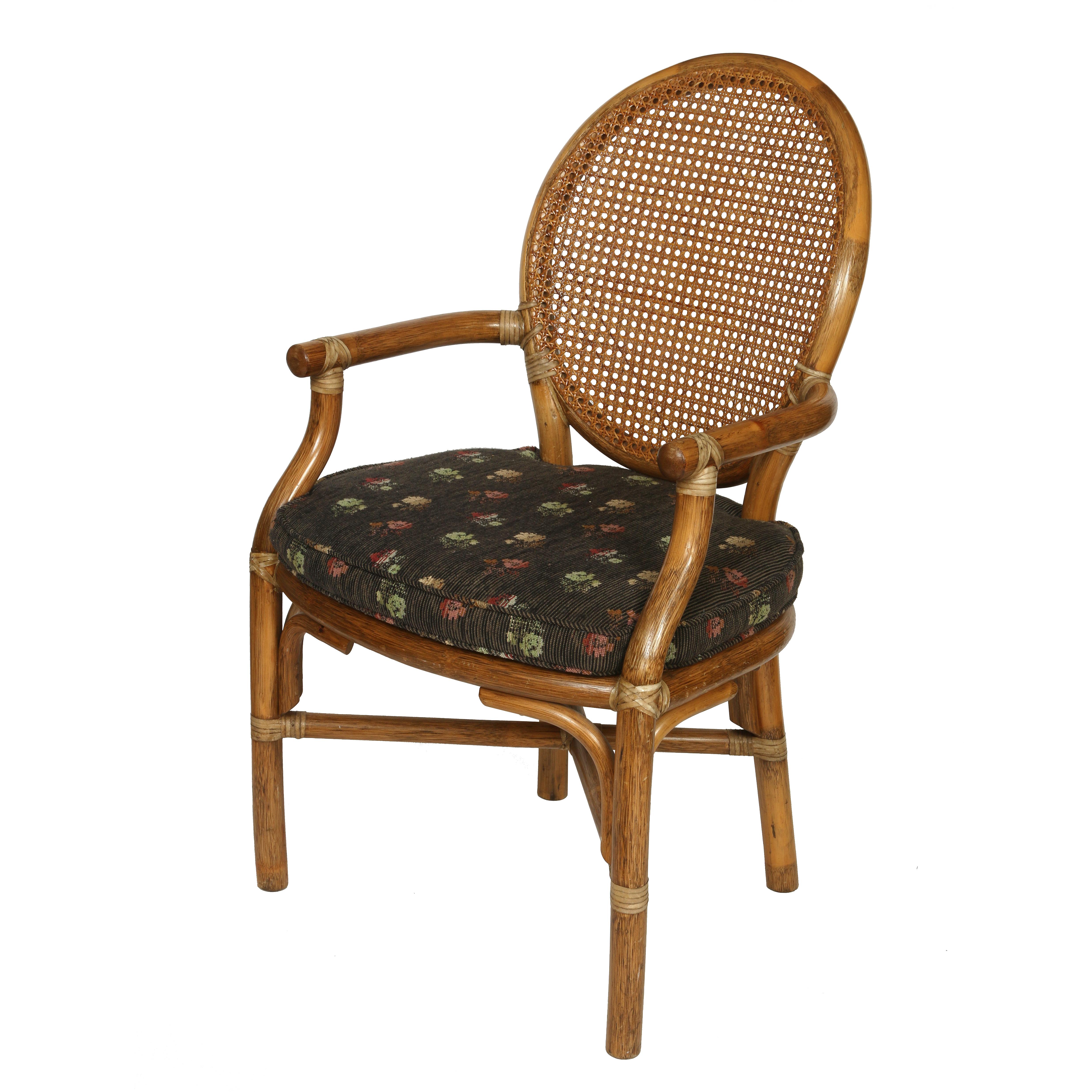 A vintage set of four caned McGuire style armchairs with oval-shaped caned back, caned seat and black floral seat cushions.  Rattan frame with curved arms and X shaped stretcher connecting straight legs