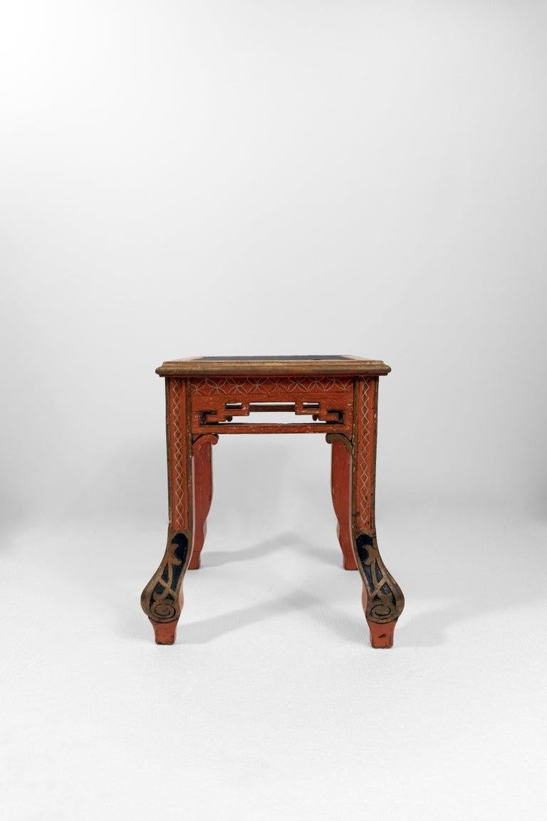 A set of four early 20th-century red-painted chinoiserie stools with hand-painted scenic panels depict idyllic pagodas and floral motifs, rendered in a rich black and gold palette that beautifully contrasts with the vibrant red frames. Intricate
