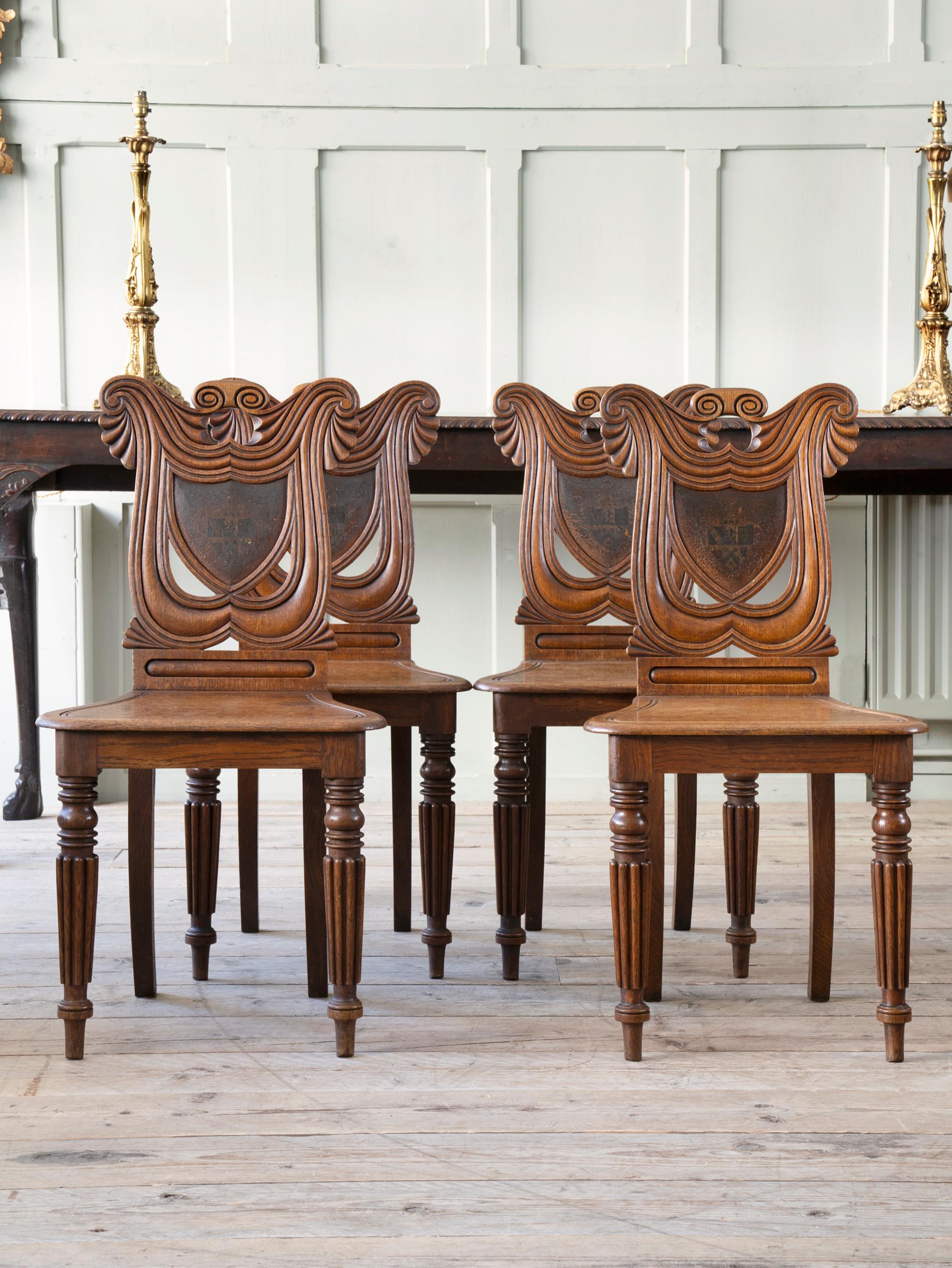 The oak back rest carved as drapery in exaggerated shield form, centered by a more formal shield with a hand painted coat of arms to each, the shaped seat supported on turned, reeded and tapering front legs with swept rears.

A fine set in largely