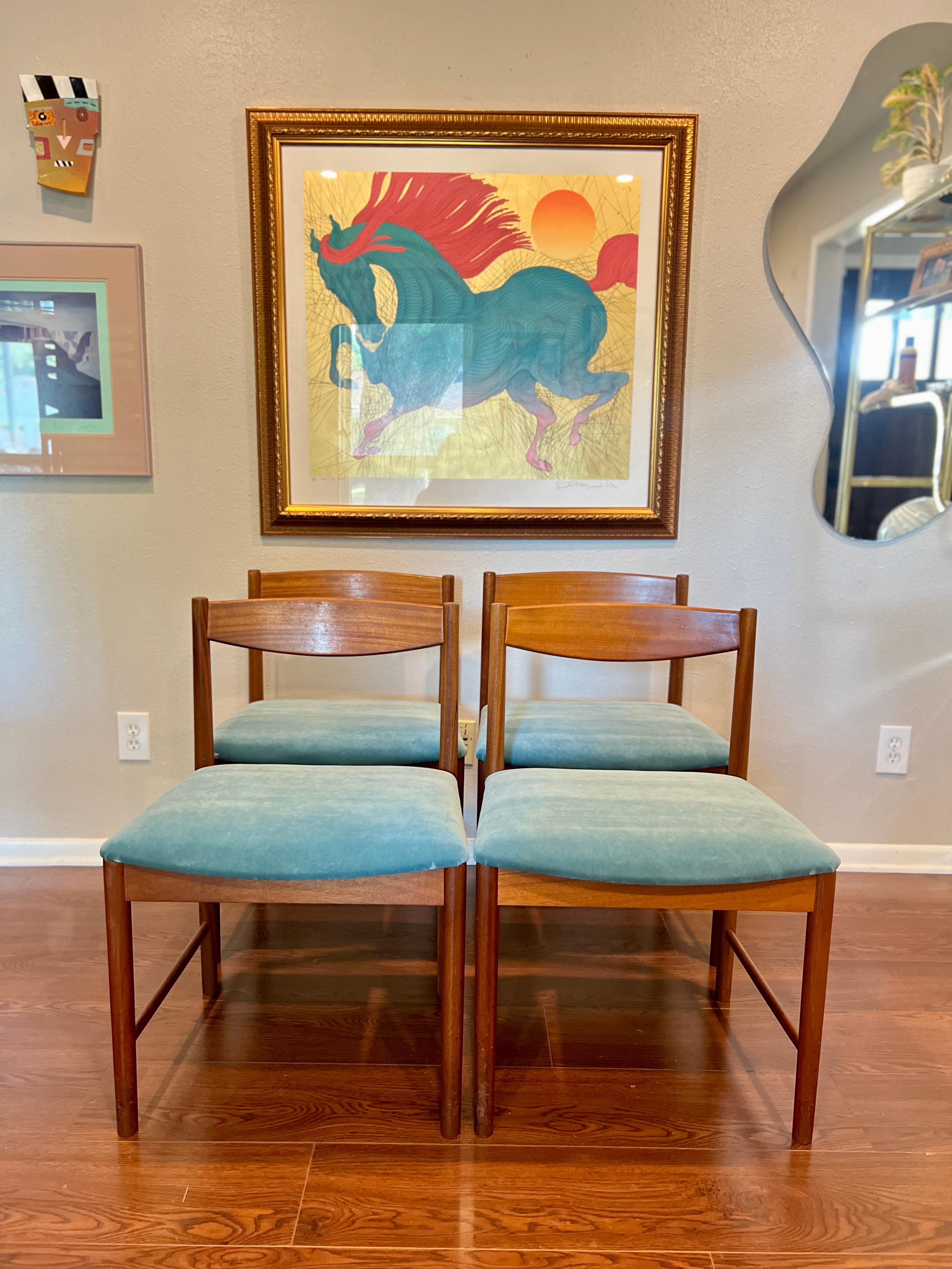 A fantastic set of four dining chairs designed by Tom Robertson for A.H McIntosh. Circa 1970s. The chairs are solid teak and have a minimalist design, with a bowed back rest and the seat cushions covered in a blue velvet. In very good condition,