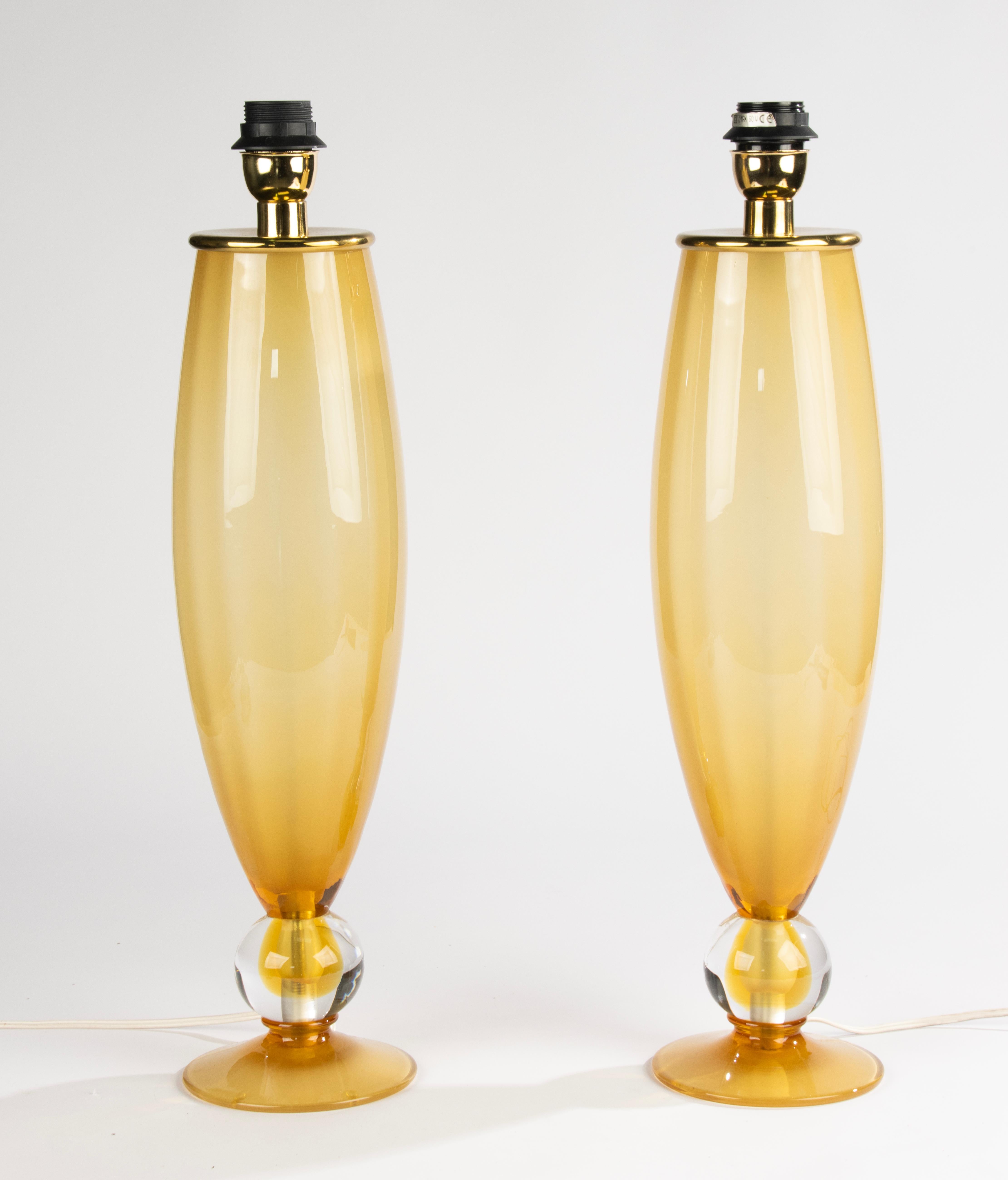 Preciosa pareja de lámparas de mesa modernas de cristal de Murano de hacia 1990.
Fabricadas en un refinado tono ámbar con una esfera de cristal transparente en la base, estas lámparas muestran una calidad y una elegancia excepcionales. Su silueta