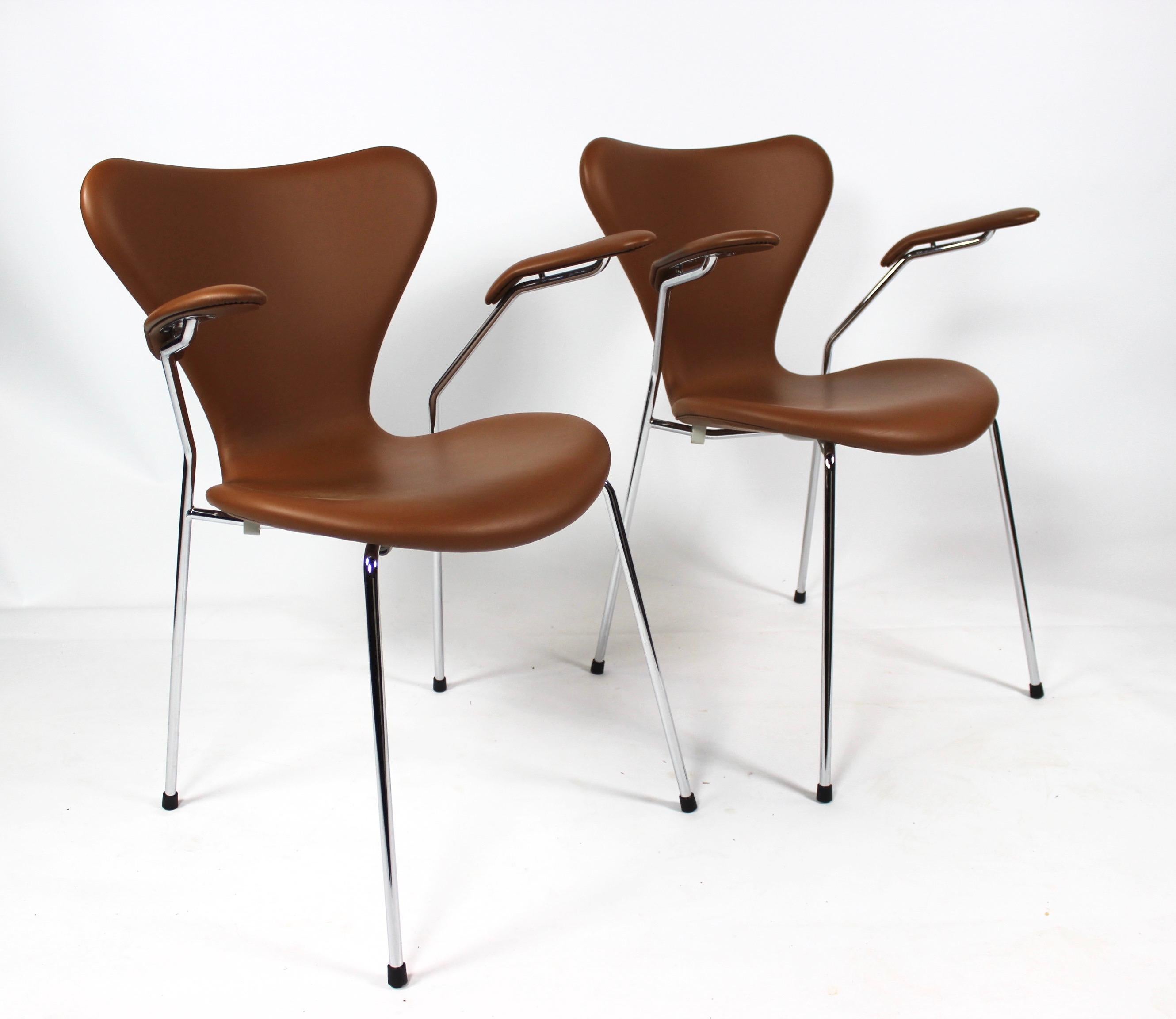 A set of seven chairs, model 3207, with armrests in cognac colored leather designed by Arne Jacobsen in 1955 and manufactured by Fritz Hansen in 2019. The chairs are in great condition.
  