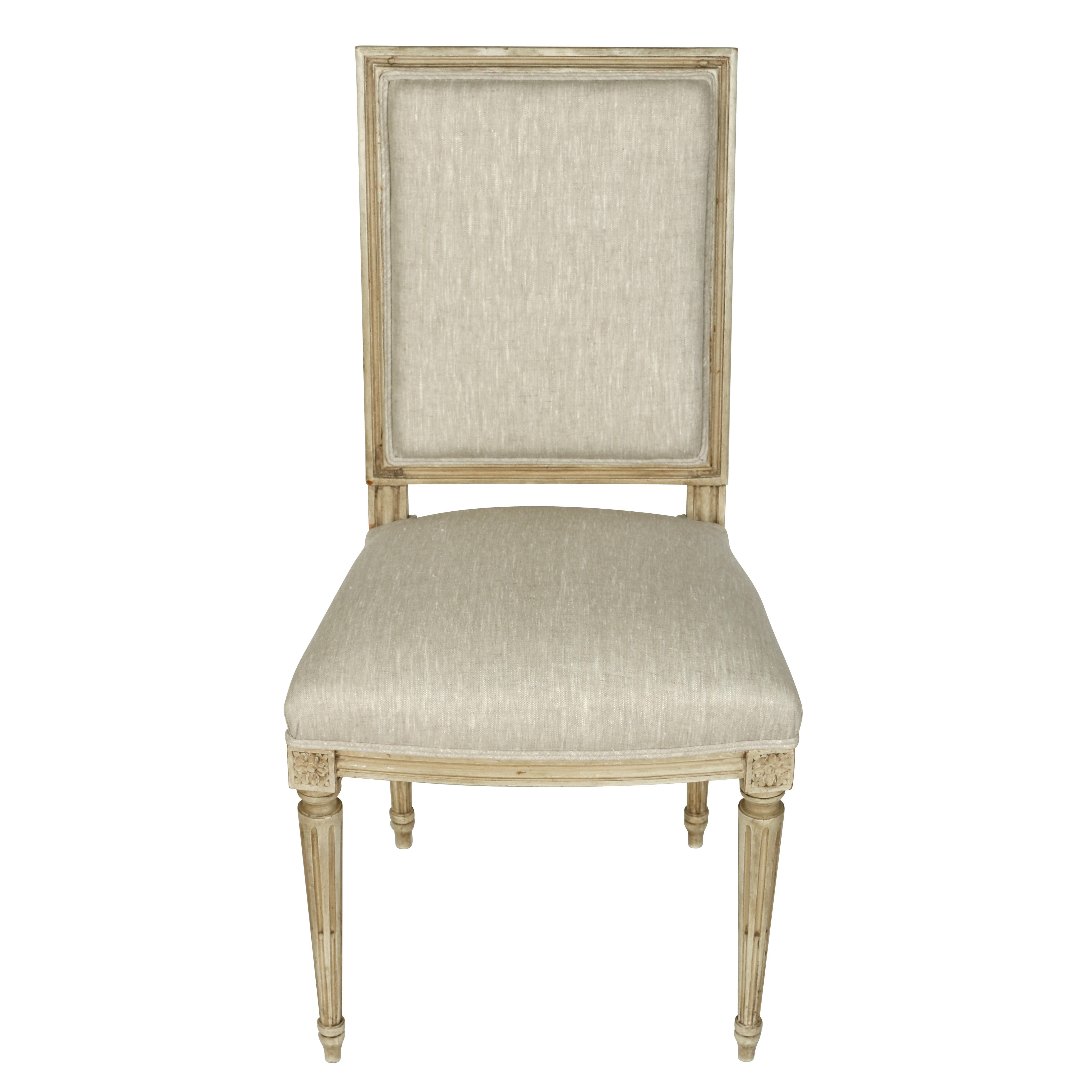 A set of dining chairs painted in a grayish white finish upholstered in a natural linen. These graceful chairs feature many of lovely details characteristic of the Louis XVI style including a square, molded back, fluted, tapered legs, and beautiful