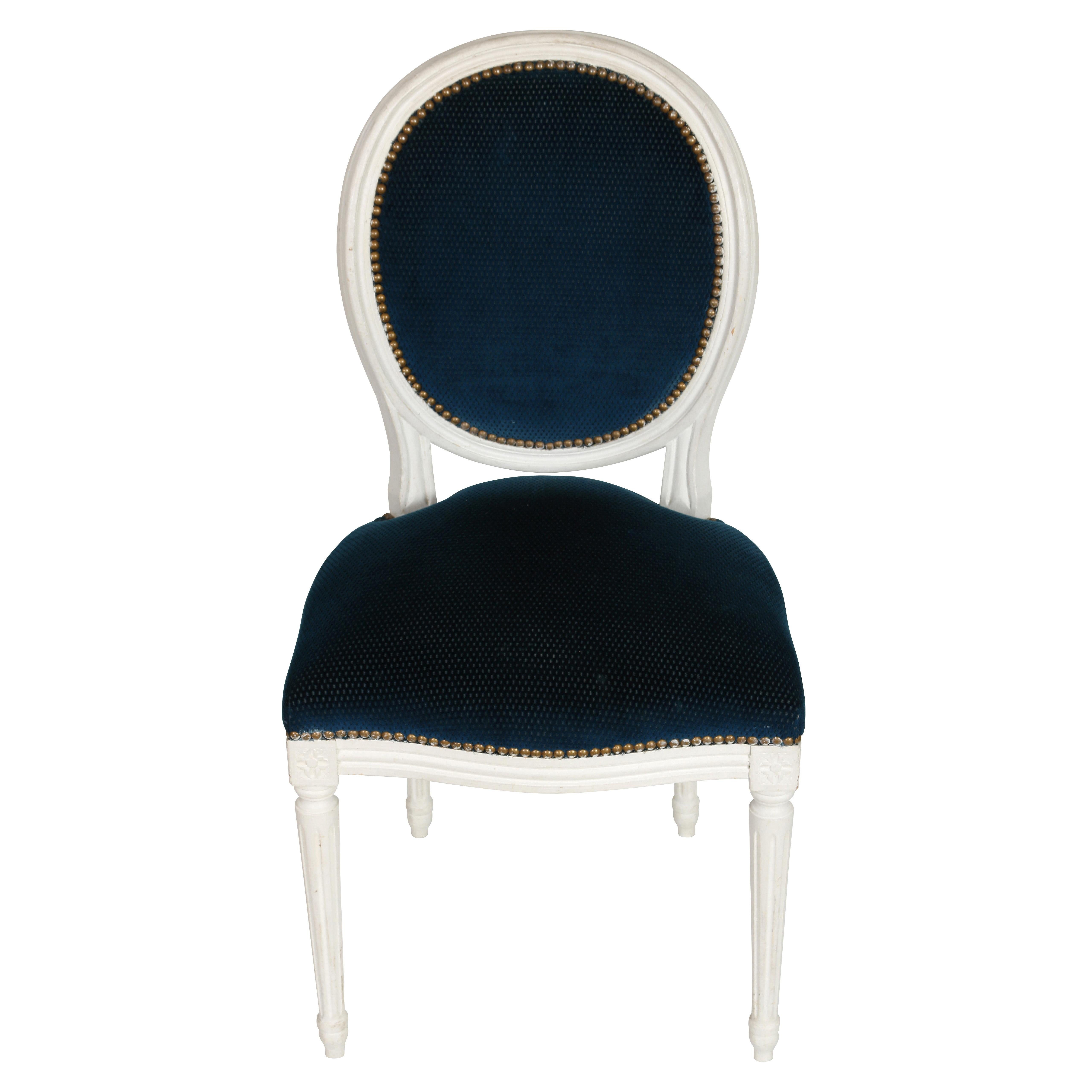 We will never tire of Louis XVI style dining chairs. With their clean, elegant lines, they can go anywhere. These oval back chairs have a white painted finish and are upholstered in a deep blue, finished with nail heads on back and seat. The carved