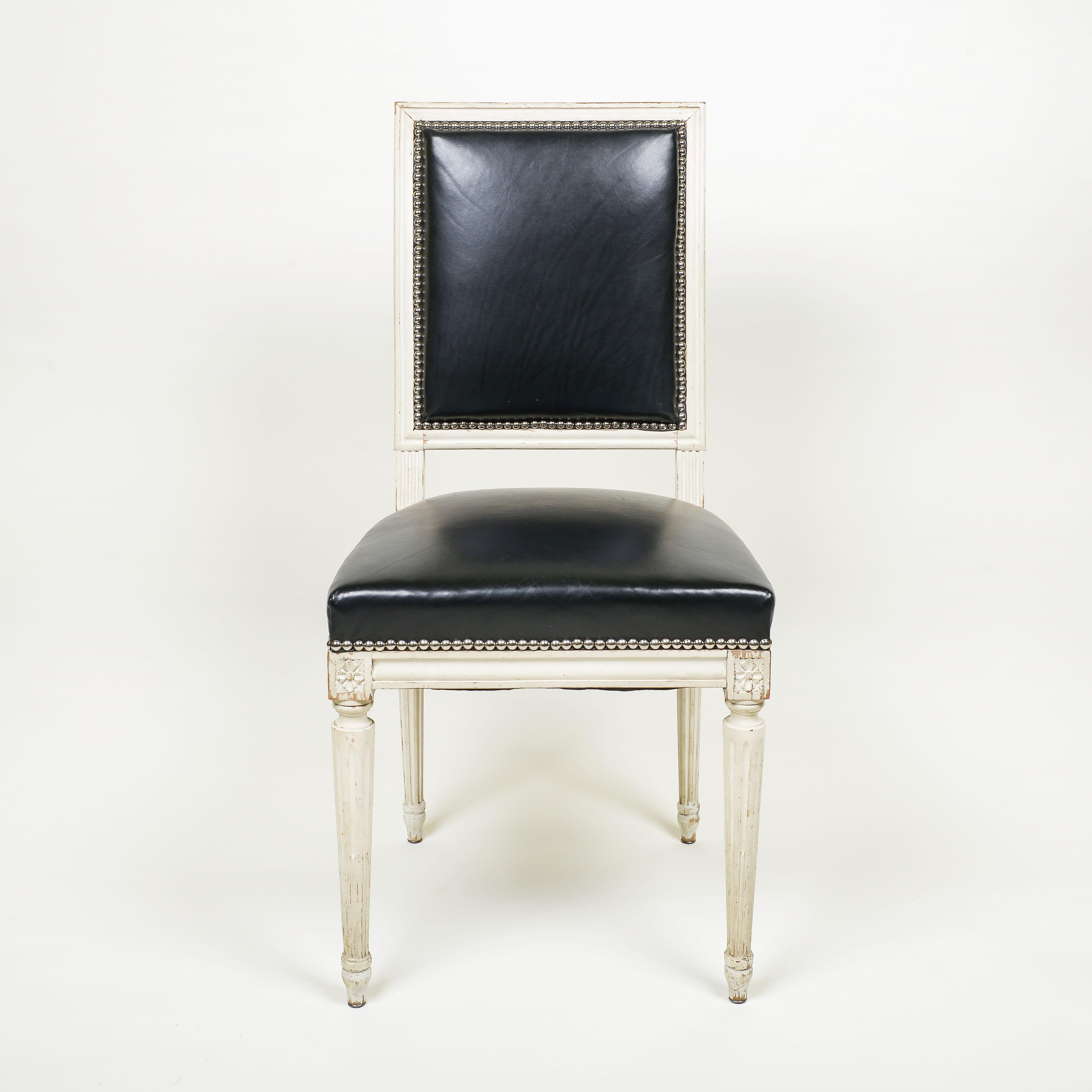 Each chair upholstered in black leather with nailhead trim; raised on fluted, round tapering legs.