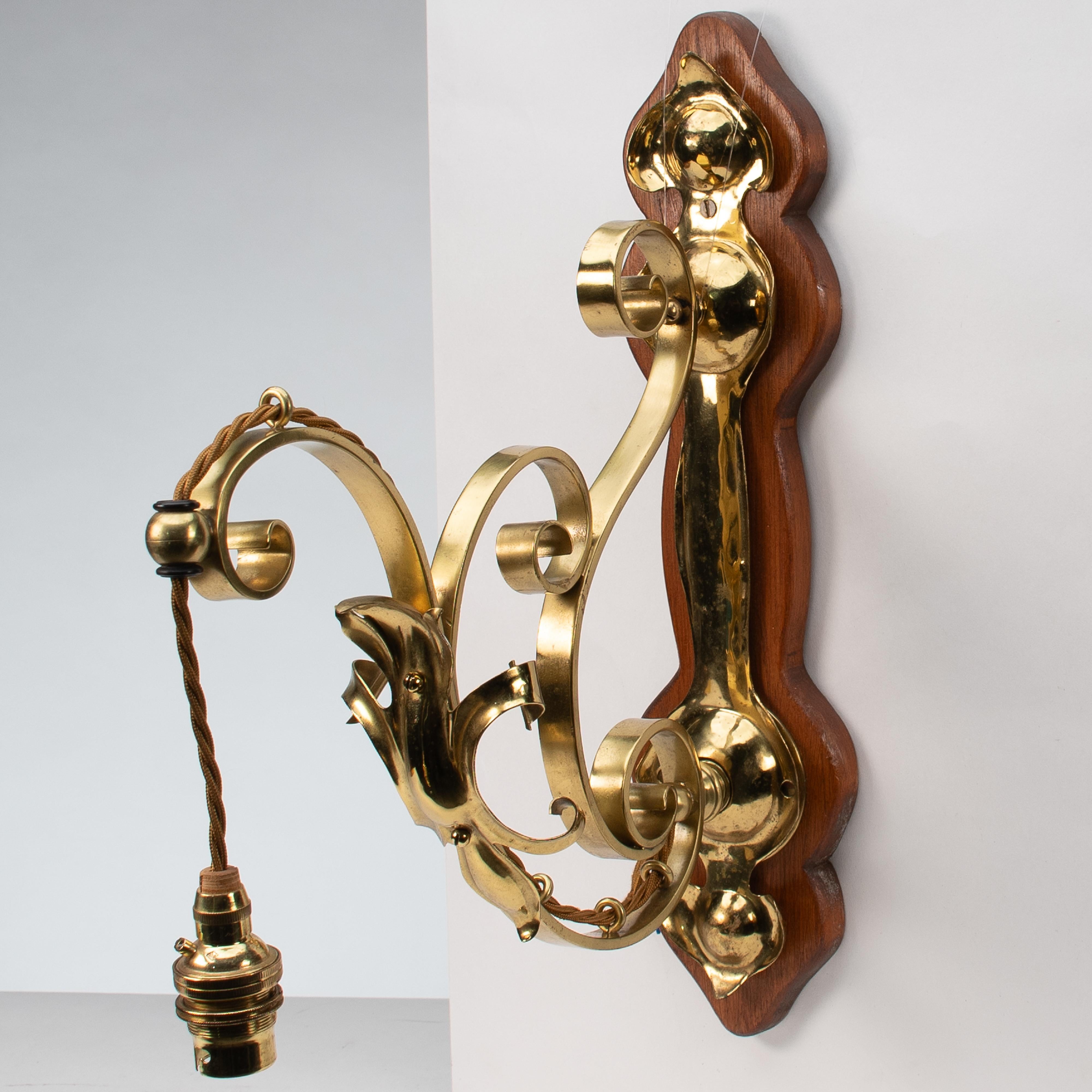 A set of three Arts and Crafts brass wall lights with walnut backplates.
