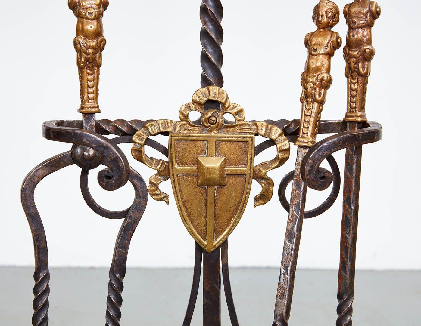 A well-crafted set of three substantial fireplace tools comprising fork, shovel and tongs, in black iron with twisted shafts and handles of bronze cherubs on ram's heads, in a custom conforming stand, having twisted iron central spine with outer