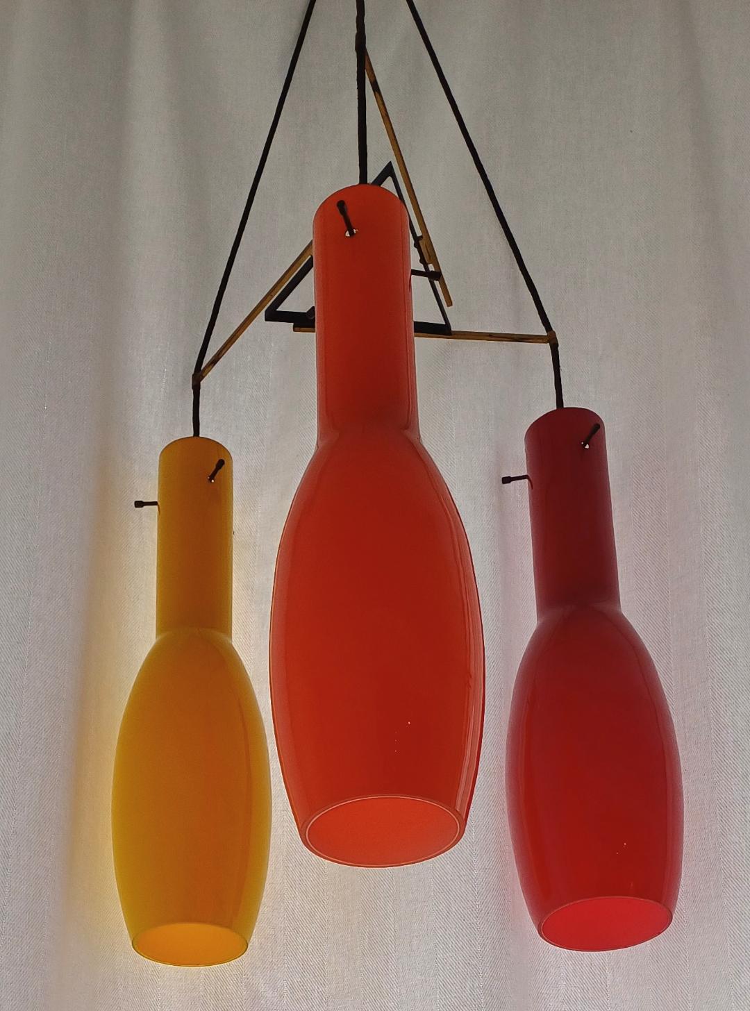 Un ensemble de trois plafonniers en verre de Murano, vers les années 1950, en trois couleurs différentes : rouge, jaune et orange. Monté dans un cadre métallique. Les dimensions du verre sont de 47 cm de haut et de 9,5 cm de diamètre.