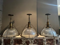 A Set Of Three Industrial Style Burnished Brass and Holophane Glass Pendants
