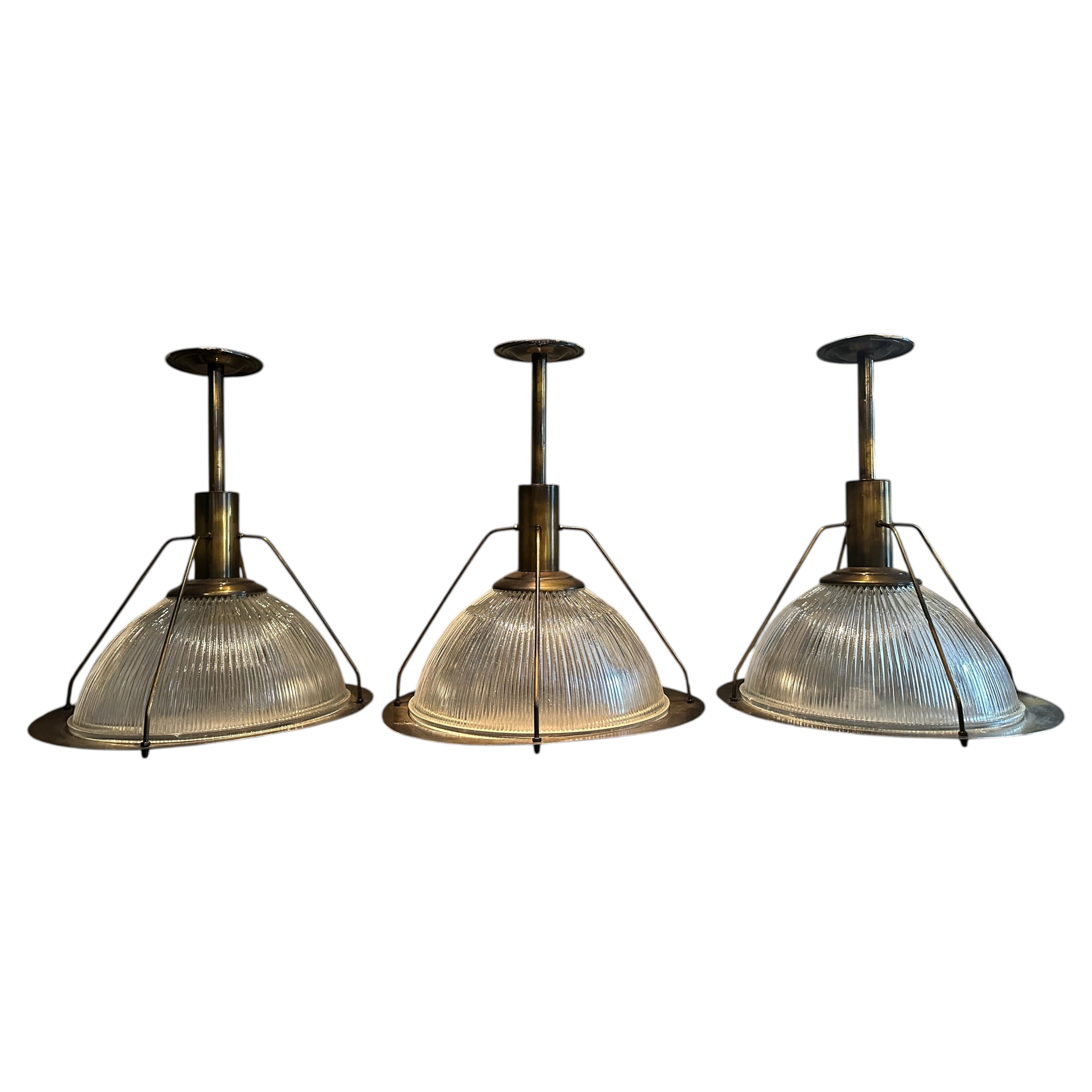 A Set Of Three Industrial Style Burnished Brass and Holophane Glass Pendants For Sale