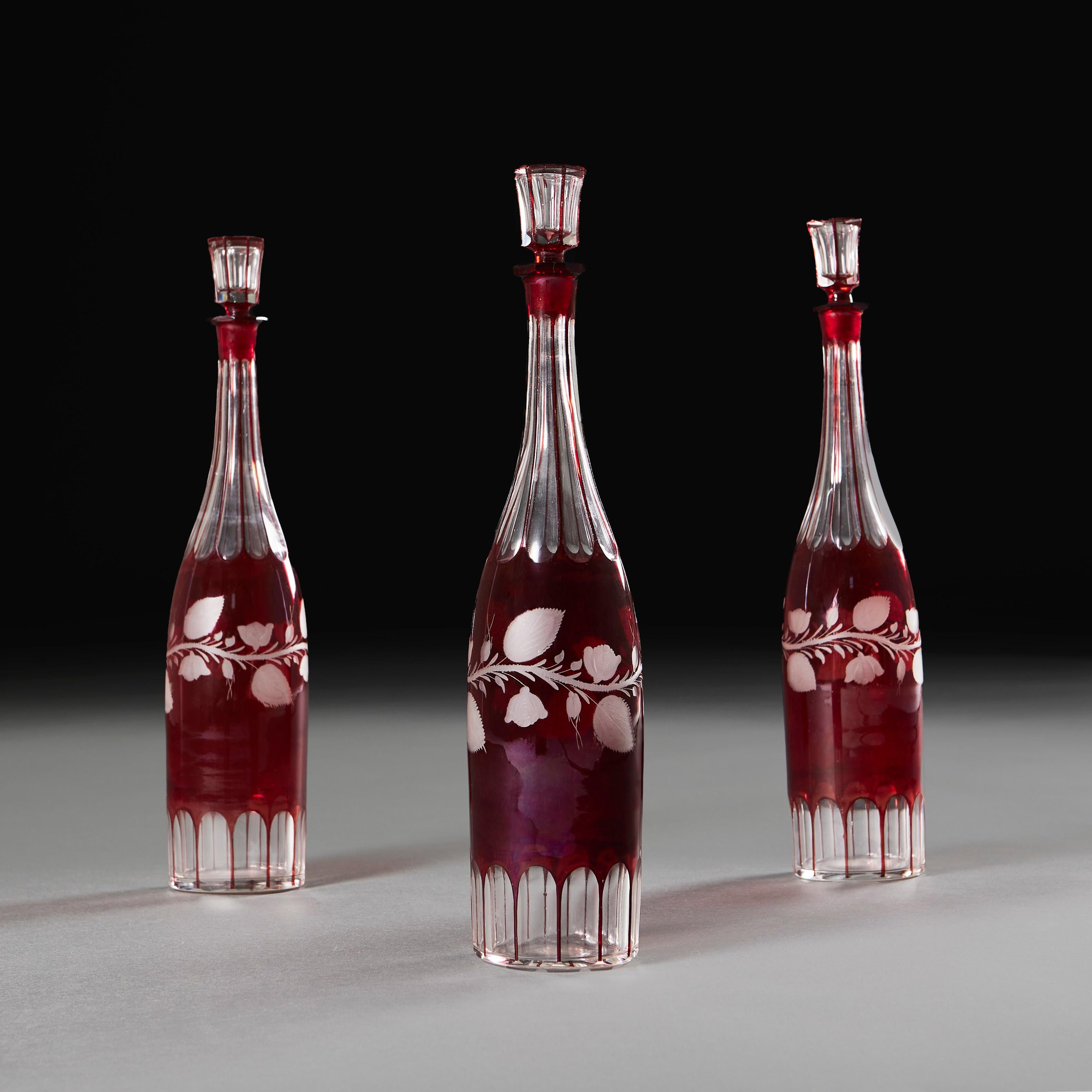 England, circa 1870
A set of three late nineteenth century red cut glass spirit decanters, the bodies engraved with scrolling vines, with faceted bases and stoppers.