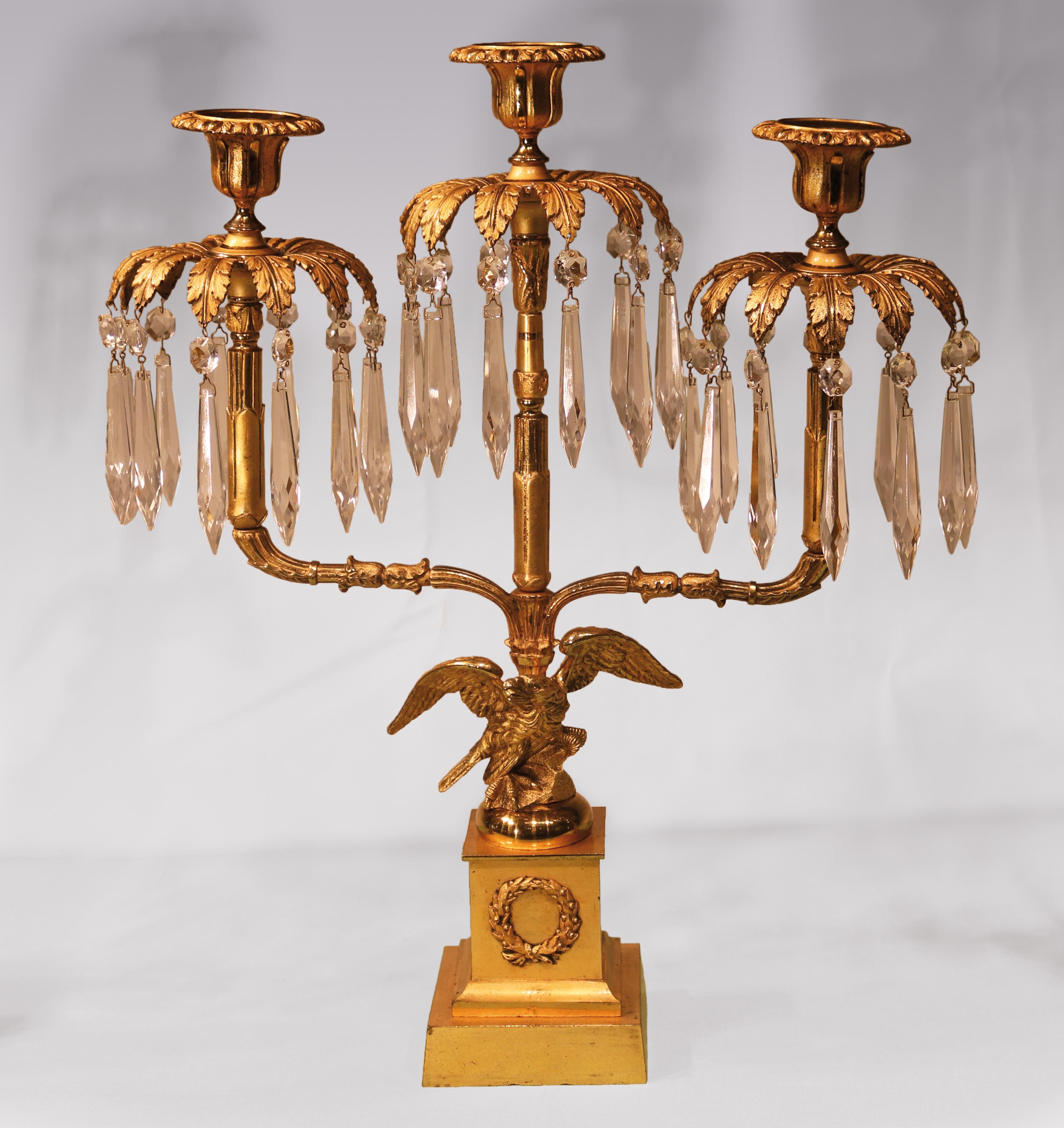 An unuusual set of large early 19th century Regency period bronze and ormolu lustre candlesticks, consisting of two singles and one triple, having lotus leaf sconces above acanthus canopies with tall stems held by well-caste eagles, raised on square