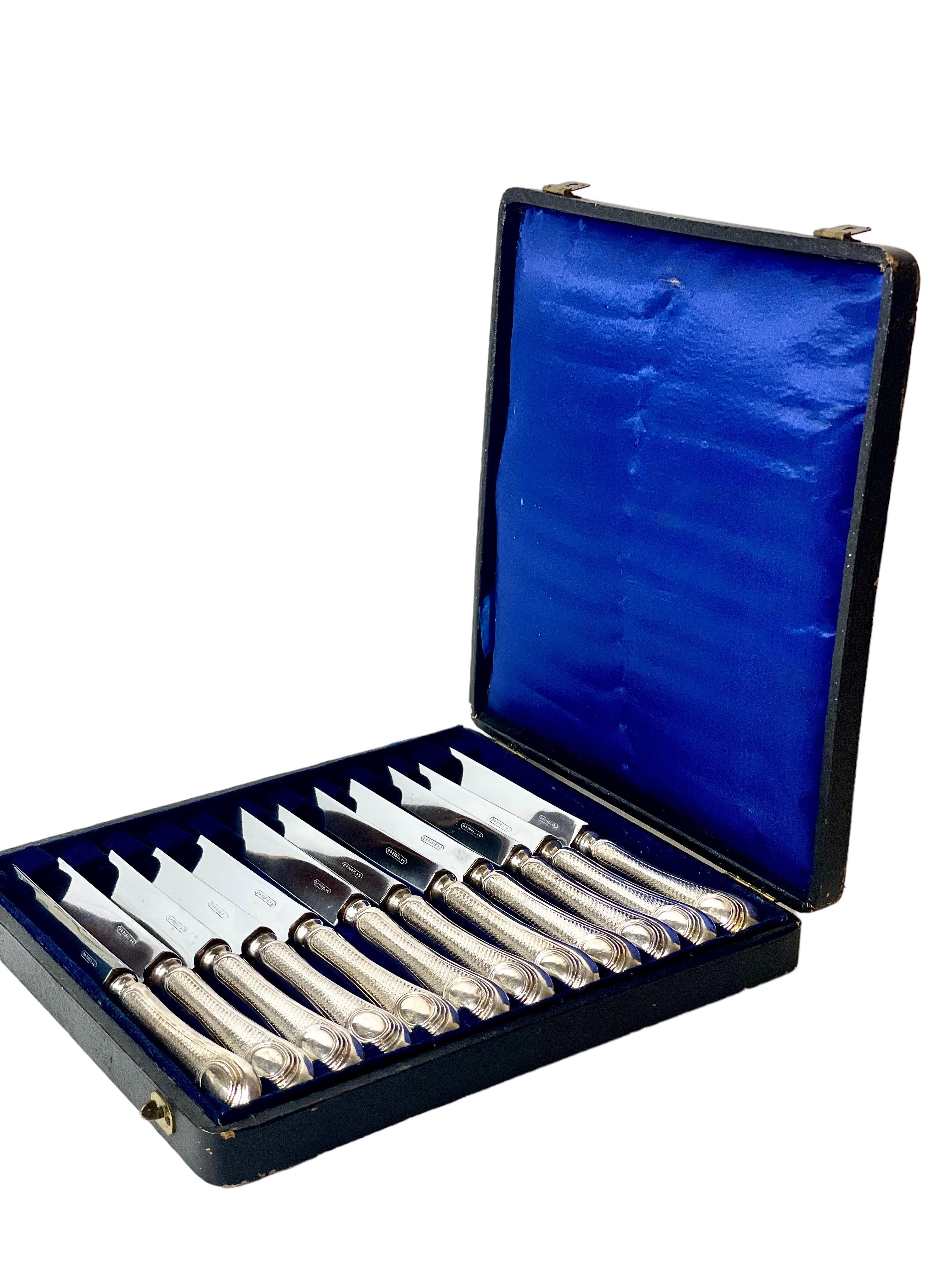 A set of twelve antique sterling silver 'Entremet' knives, the blades hallmarked with the 950/100 Minerva head stamp and offered in their original blue silk-lined presentation case. The handles are silver mounted, and feature an intricate