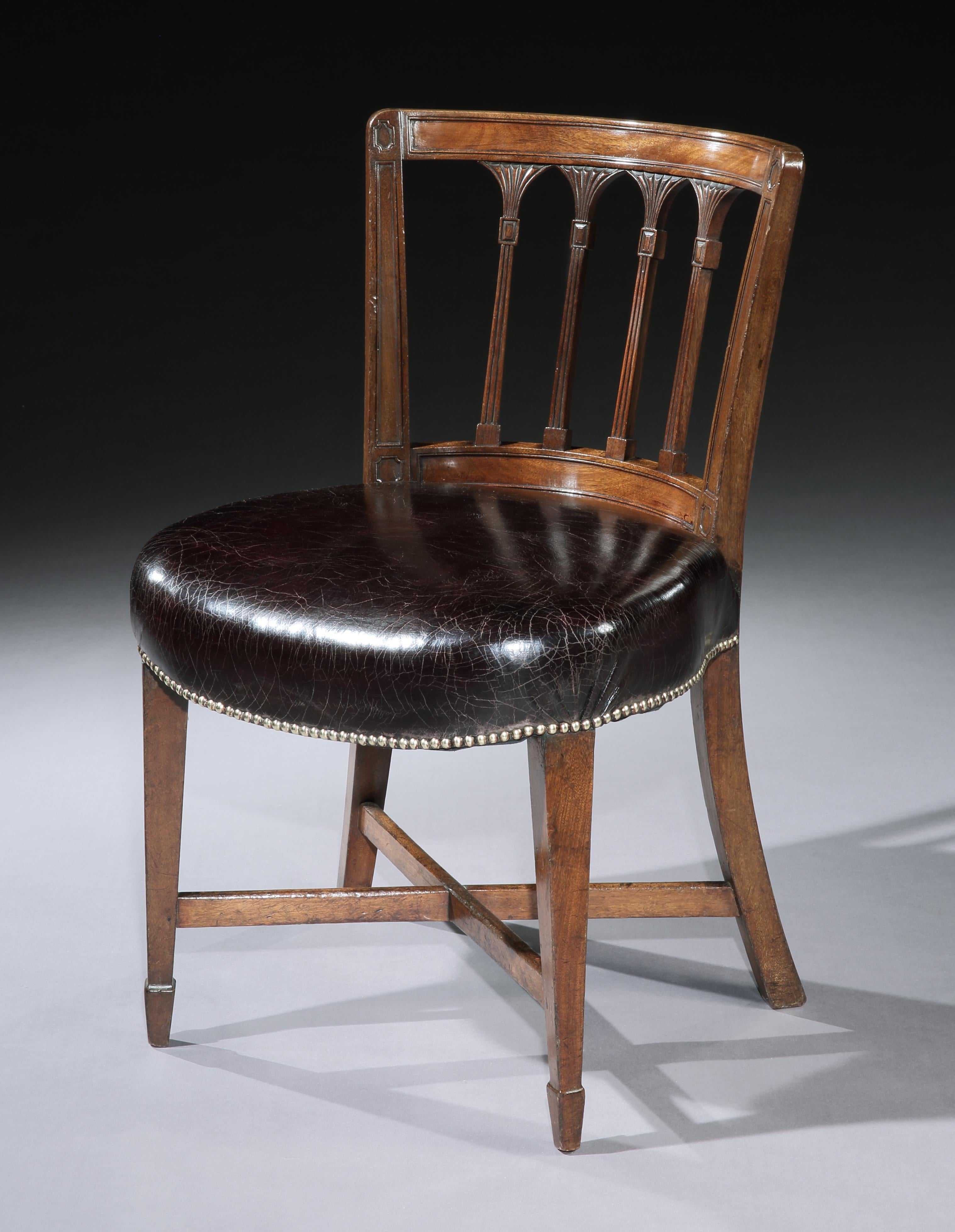 An unusual set of twelve late George III brown mahogany tub library chairs, the concave shaped backs with panelled uprights, outside four fishtail splats, above a round overstuffed seat, covered in maroon hide, resting on square tapered legs with