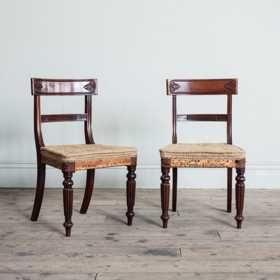 Each with a tablet top rail carved with anthemion on either side above a reeded horizontal splat and fluted uprights, on hessian covered seat, above turned and reeded tapering front legs. The overall design of this elegant set of dining chairs