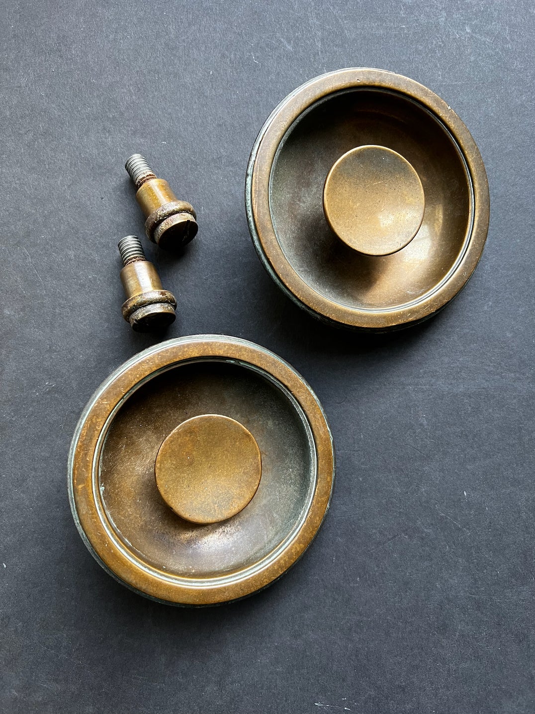 A pair of circular bronze inset handles with nice aged patina. 20th century, found in England.

The handles each comprise two parts - and outer dish with an inner knob - all held in place by a heavy bolt on the reverse side. The outer dish is