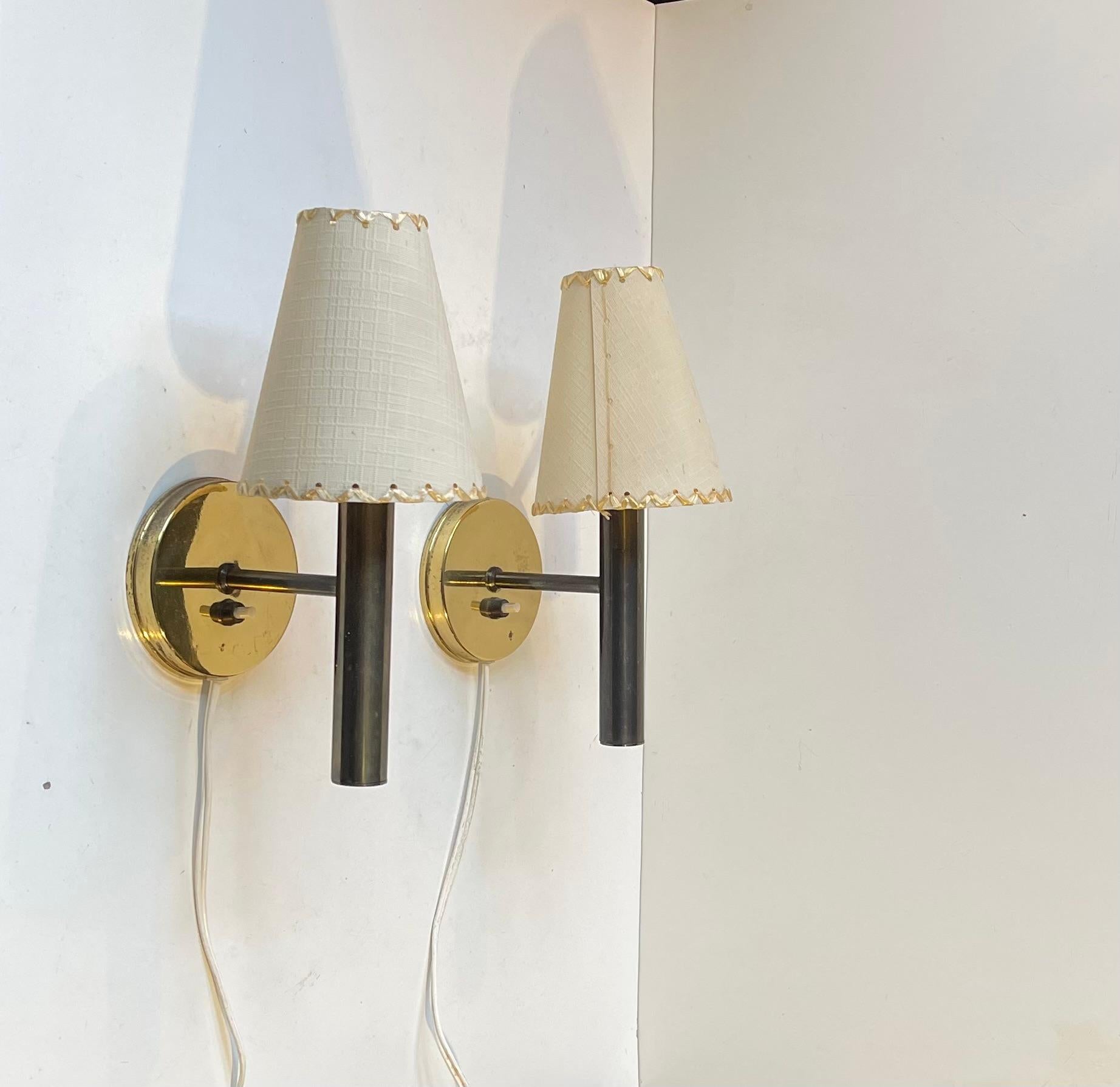 A pair of fixed wall sconces designed by Svend Mejlstrøm in Denmark during the 1960s and made by MS Belysning during the 1970s. The set is made from polished brass and comes with period shades. 

Measurements: H: 25 cm, Dept: 14 cm, Diameter: 11 cm