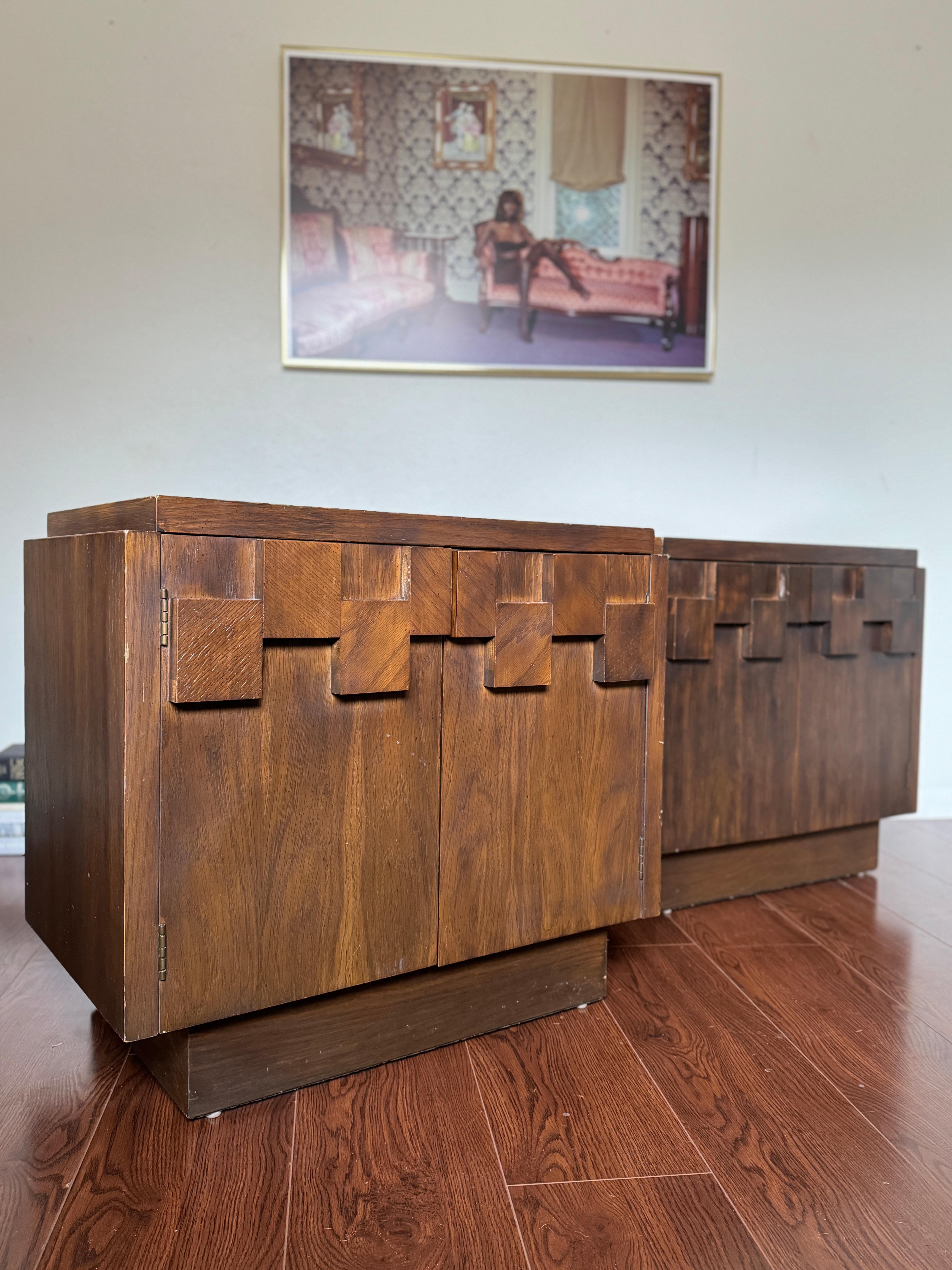A set of vintage mid century modern nighstands by Lane Furniture, circa 1970s. Styled after designer Paul Evans, these nightstands feature an iconic brutalist style with a heavy oak wood mosaic on the front doors, plinth base, and interior shelving.