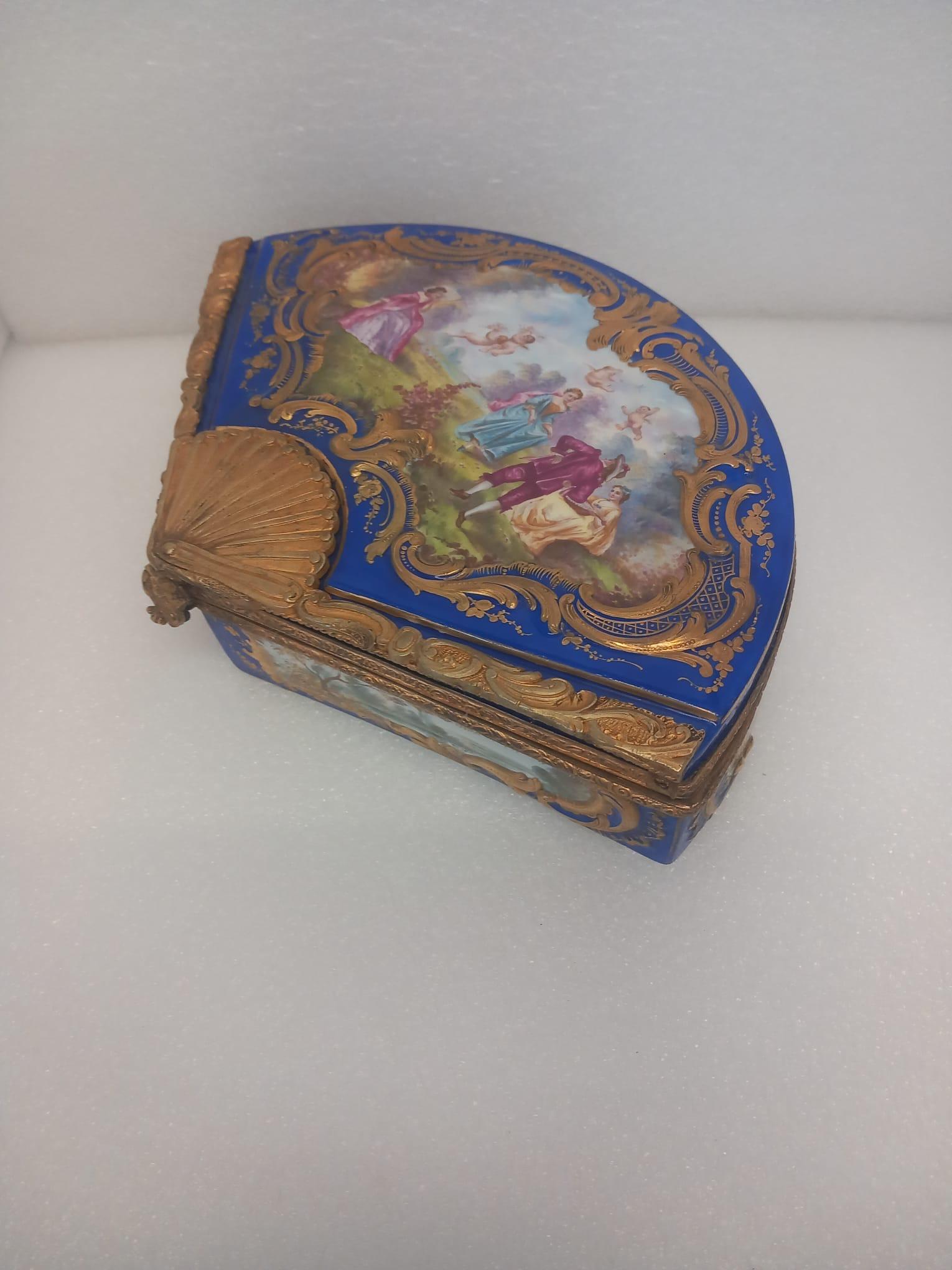 Boîte à bijoux ou coffret en porcelaine en forme d'éventail, de style Sèvres, datant du dernier quart du XIXe siècle.
Peint à la main avec des scènes allégoriques de style Watteau représentant trois femmes dans un paysage courtisées par un cavalier,