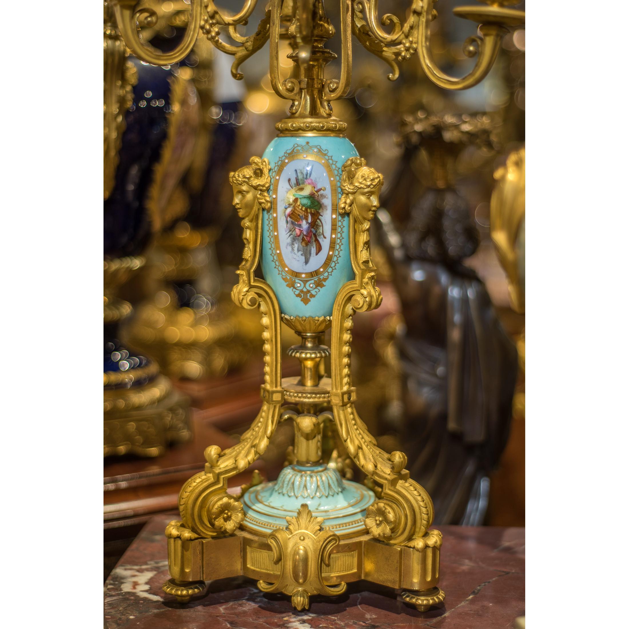 Un ensemble sophistiqué d'horloge Napoléon III en porcelaine de Sèvres monté en bronze doré par Grohé Paris avec un boîtier d'horloge ovoïde monté sur un masque de bélier soutenu par deux putti sur une base façonnée avec des panneaux en porcelaine