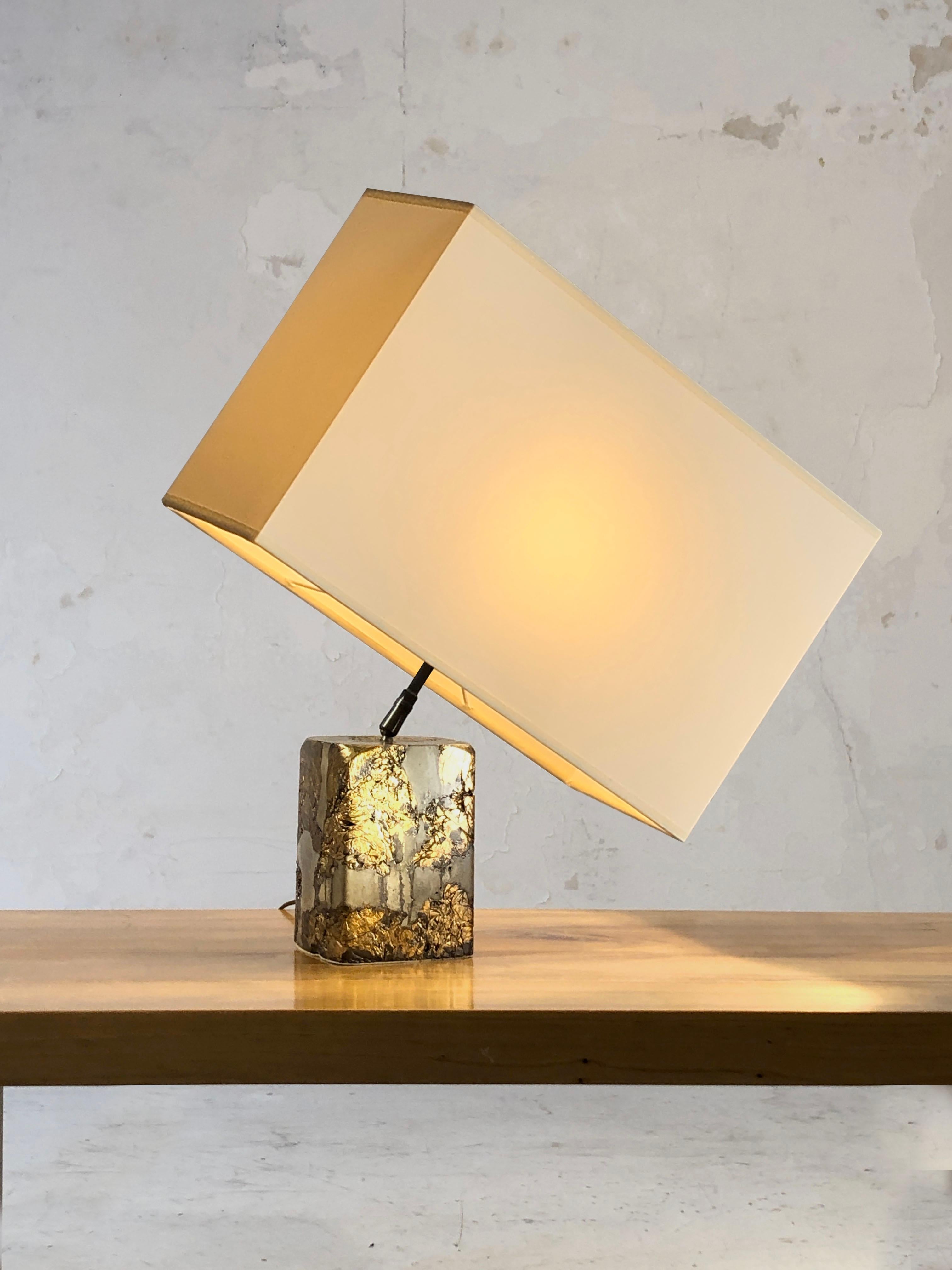 A sculptural cubic table lamp, Post-Modernist, Shabby-Chic, Neoclassical, massive cubic compression of golden and silver metals, with an orientable rectangular horizontal shade, allowing various positions, to be attributed, France 1990.

This