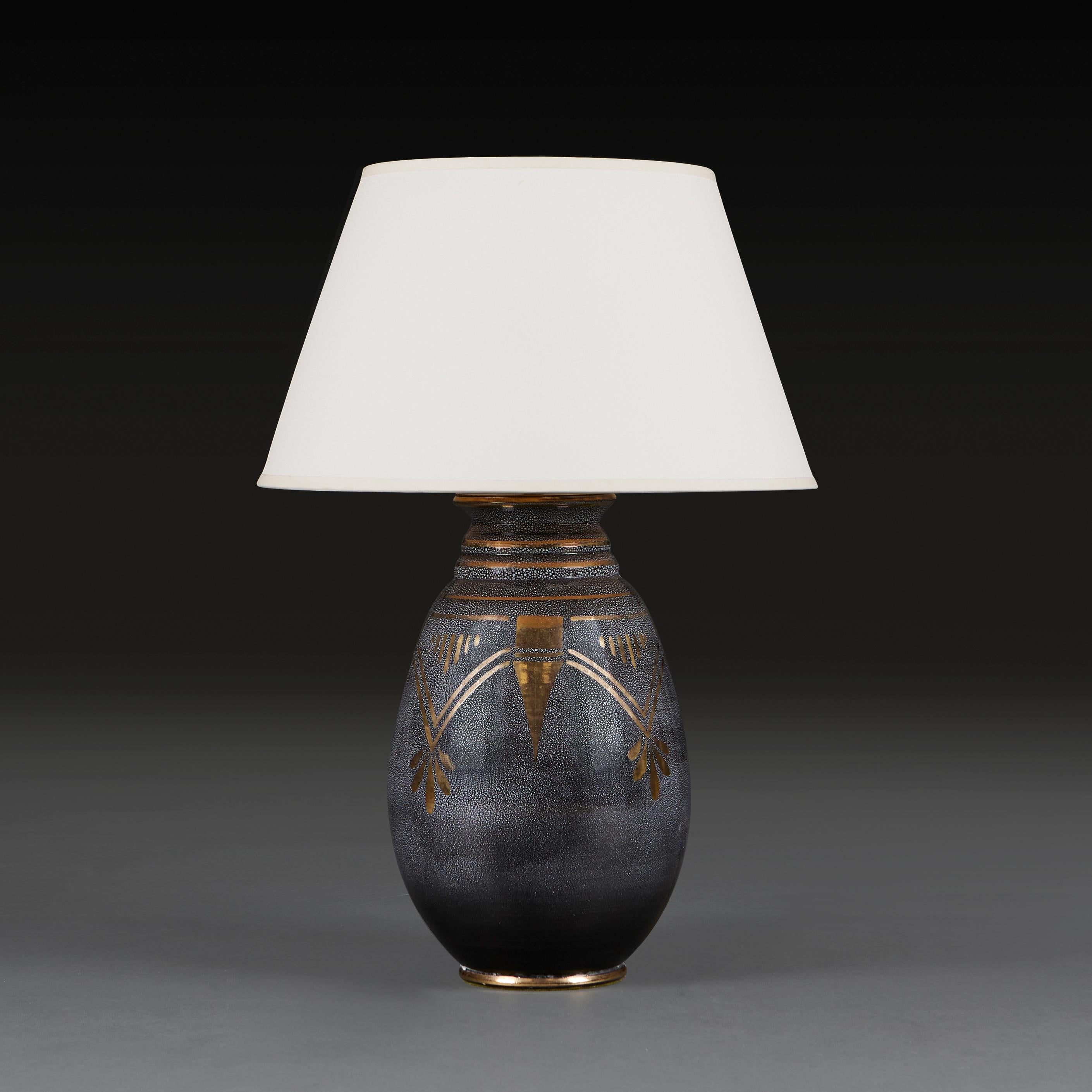 An Art Deco vase with unusual shagreen simulated grey speckled glaze, with gilt glaze overlay in geometric motives, now as a lamp. 
France, circa 1930
Height of vase   36.00cm
Height with shade   61.00cm
Diameter of base  12.00cm

Please note: Does