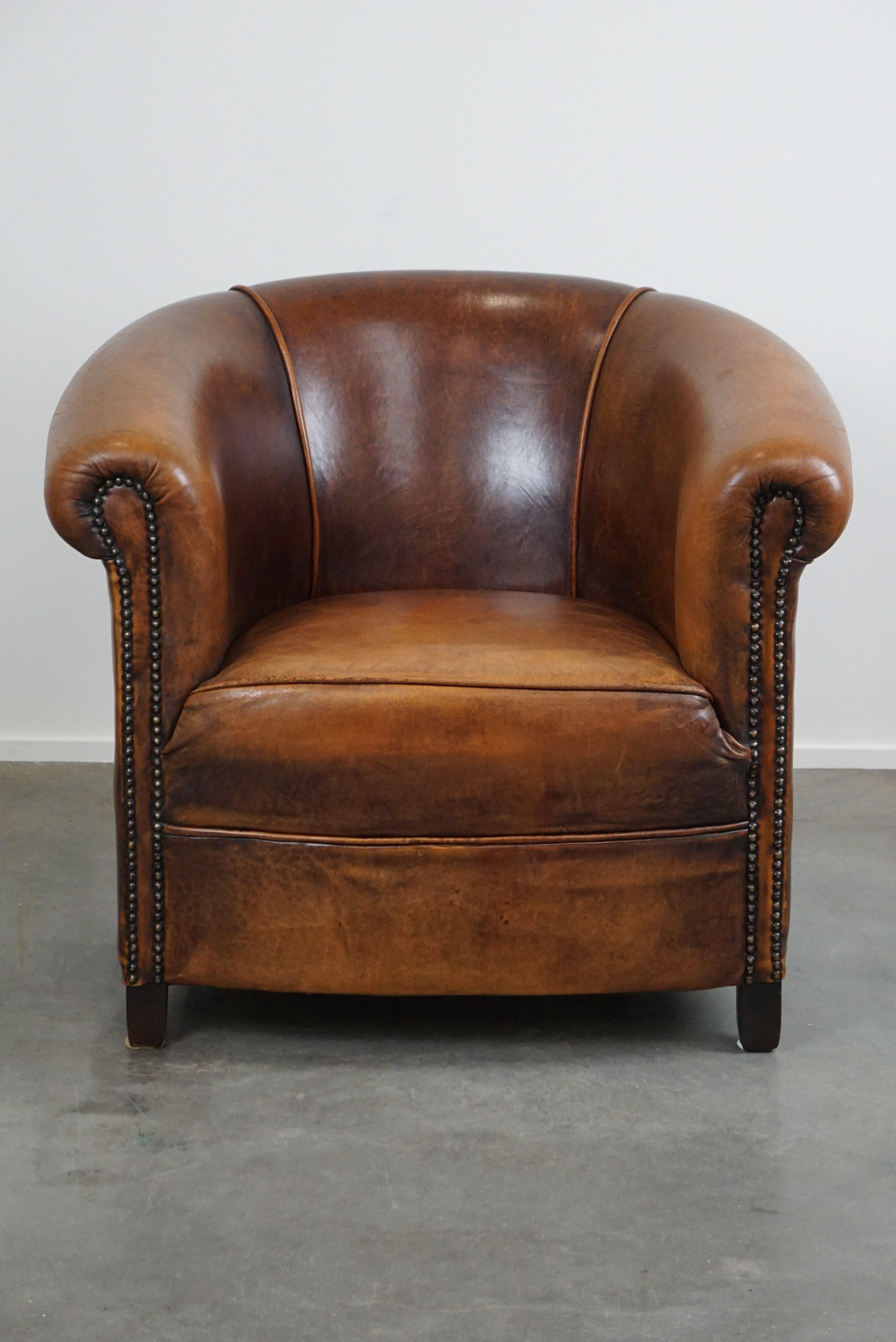Offered: this sheep leather club armchair in good condition, modest in size, with a beautiful warm cognac color.

This lovely sheep leather club armchair is in good and properly used condition, featuring a fixed seat cushion. Its modest size makes