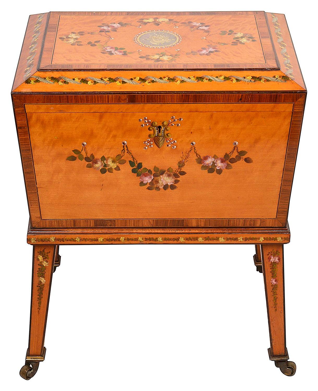 An Edwardian period, Sheraton revival satinwood and rosewood hand paint cellarette on stand, the top with a ribbon and flower frieze, swagged rose garland and a central medallion with musical instruments  The front with a  swagged floral garland.
