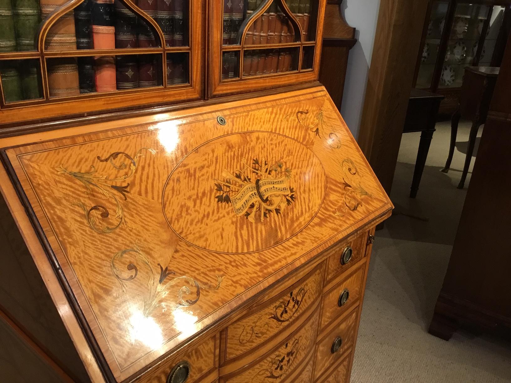 A Sheraton Revival satinwood marquetry inlaid antique bureau bookcase by Maple & Co, London. The upper bookcase section has a fine marquetry anthemion inlaid frieze above twin astragal glazed doors and having three adjustable mahogany shelves. The