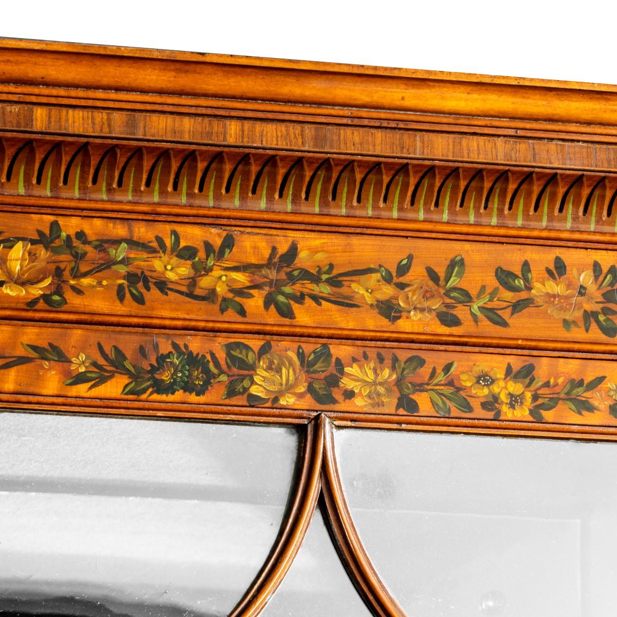A Sheraton period West Indian satinwood secretaire bookcase, with later painted Victorian decoration and mirror backs, of tall rectangular form, the upper section with two doors of glazed arches enclosing three adjustable shelves, the base with five